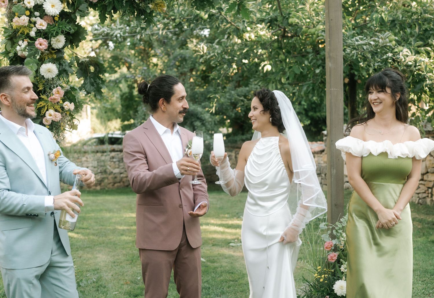 Wedding party members share joyful moments while dancing and laughing together in a lush garden setting.