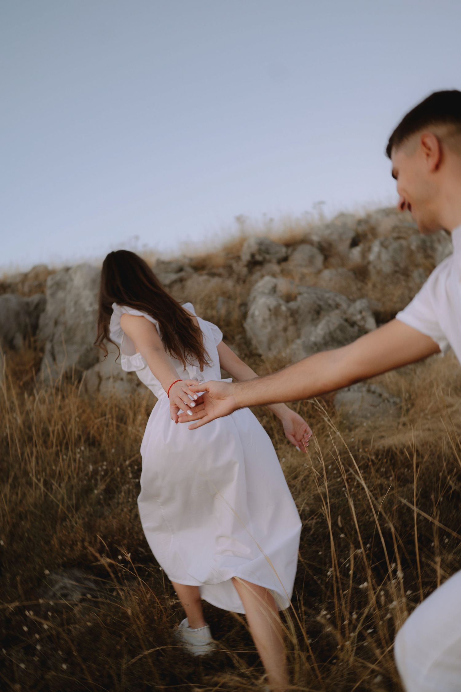 A couple holds hands tenderly in a field of tall grass during golden hour.