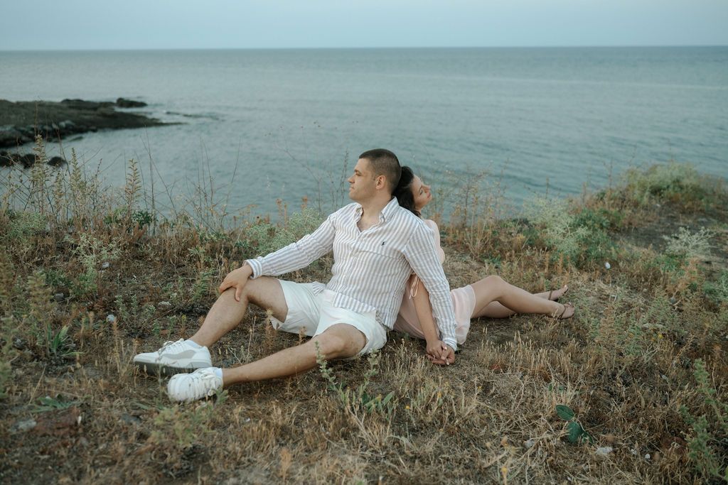 Person in white clothing lying on coastal grass overlooking ocean in multiple artistic poses at sunset.