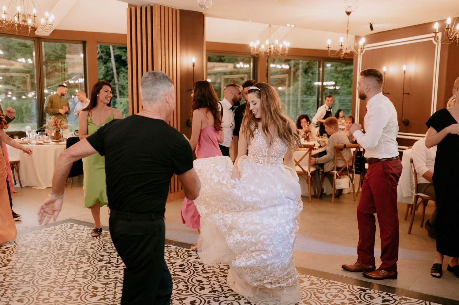 Wedding guests dance and celebrate on an elegant dance floor with warm lighting and wooden accents.