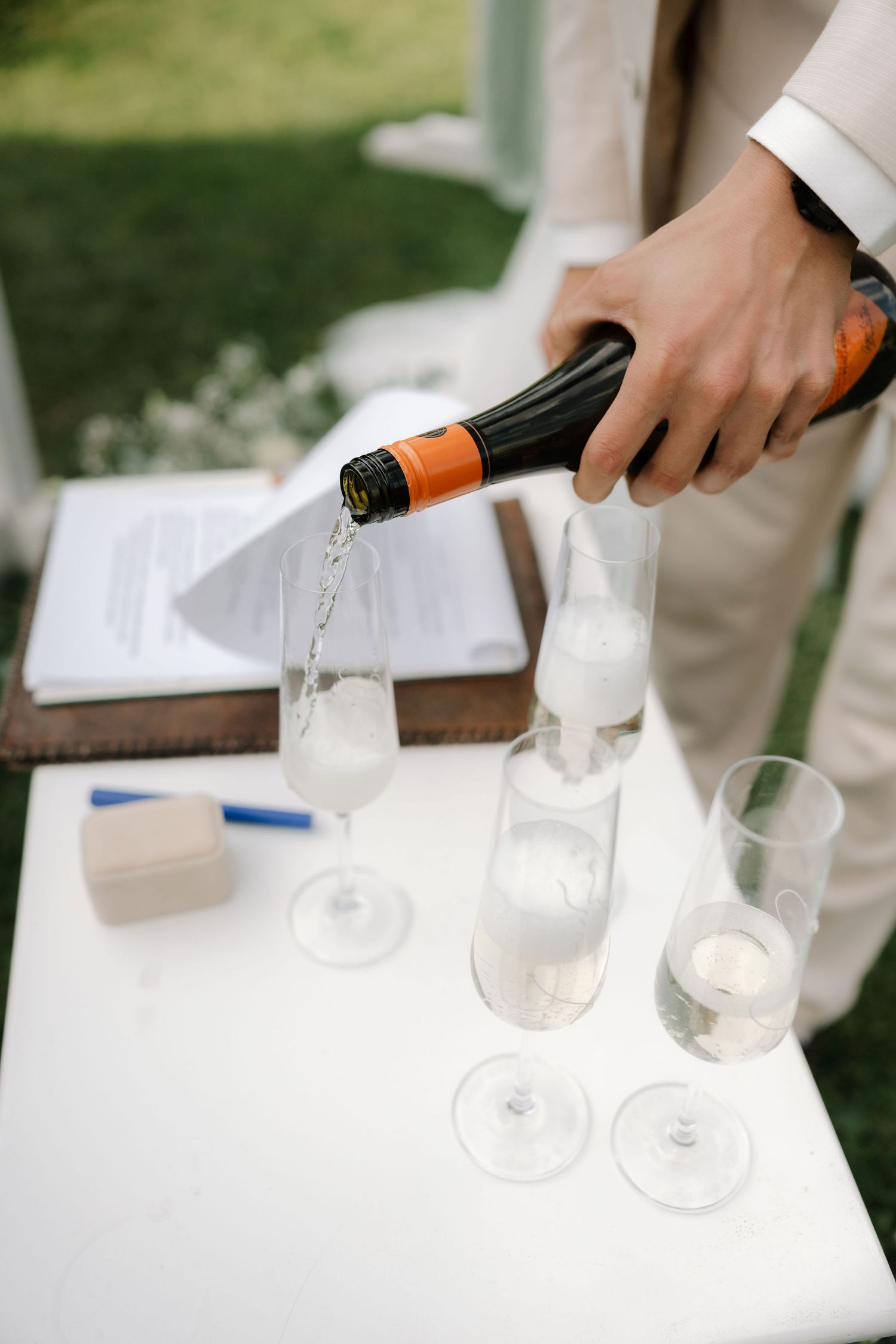 Champagne being poured into multiple wine glasses at an outdoor event setting.