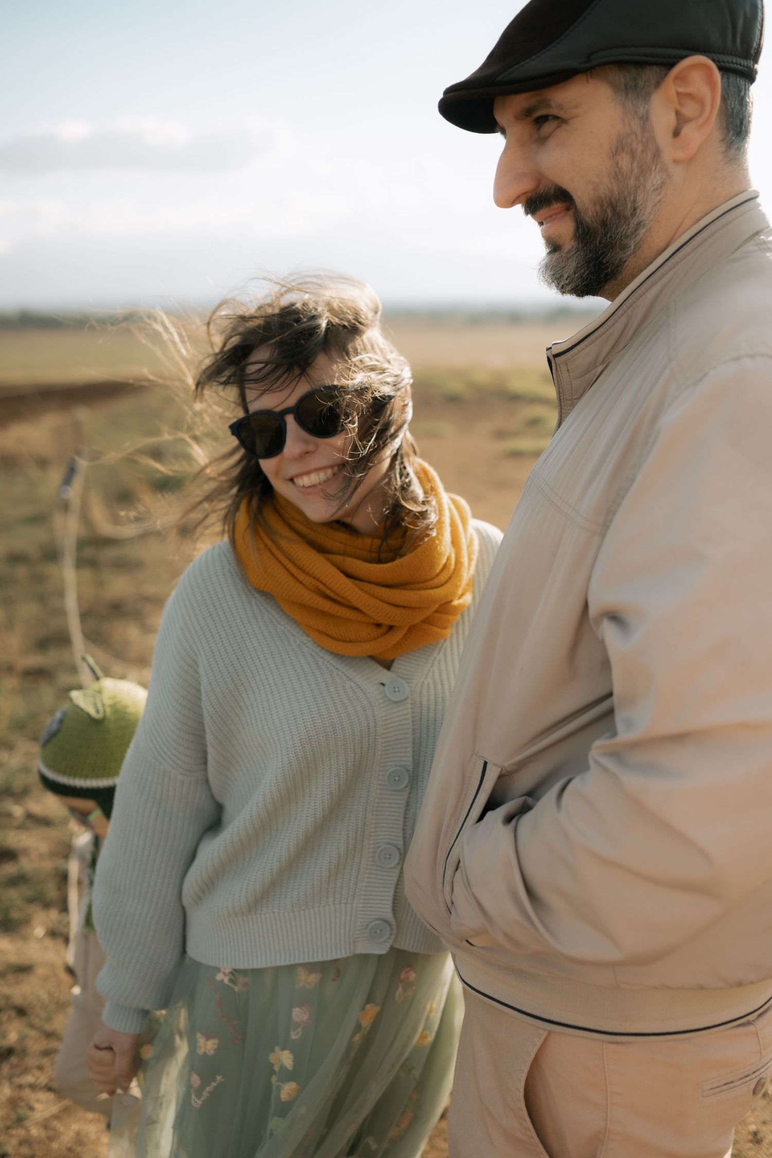Couple in casual autumn attire standing close together in a golden field at sunset.