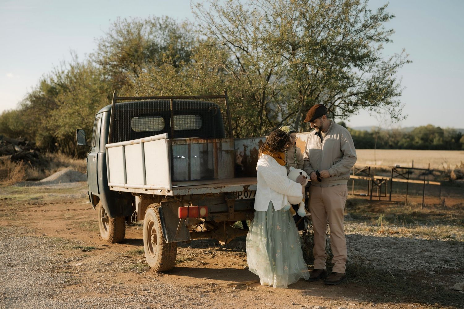 A couple stands beside a vintage farm truck in a rustic outdoor setting during golden hour.