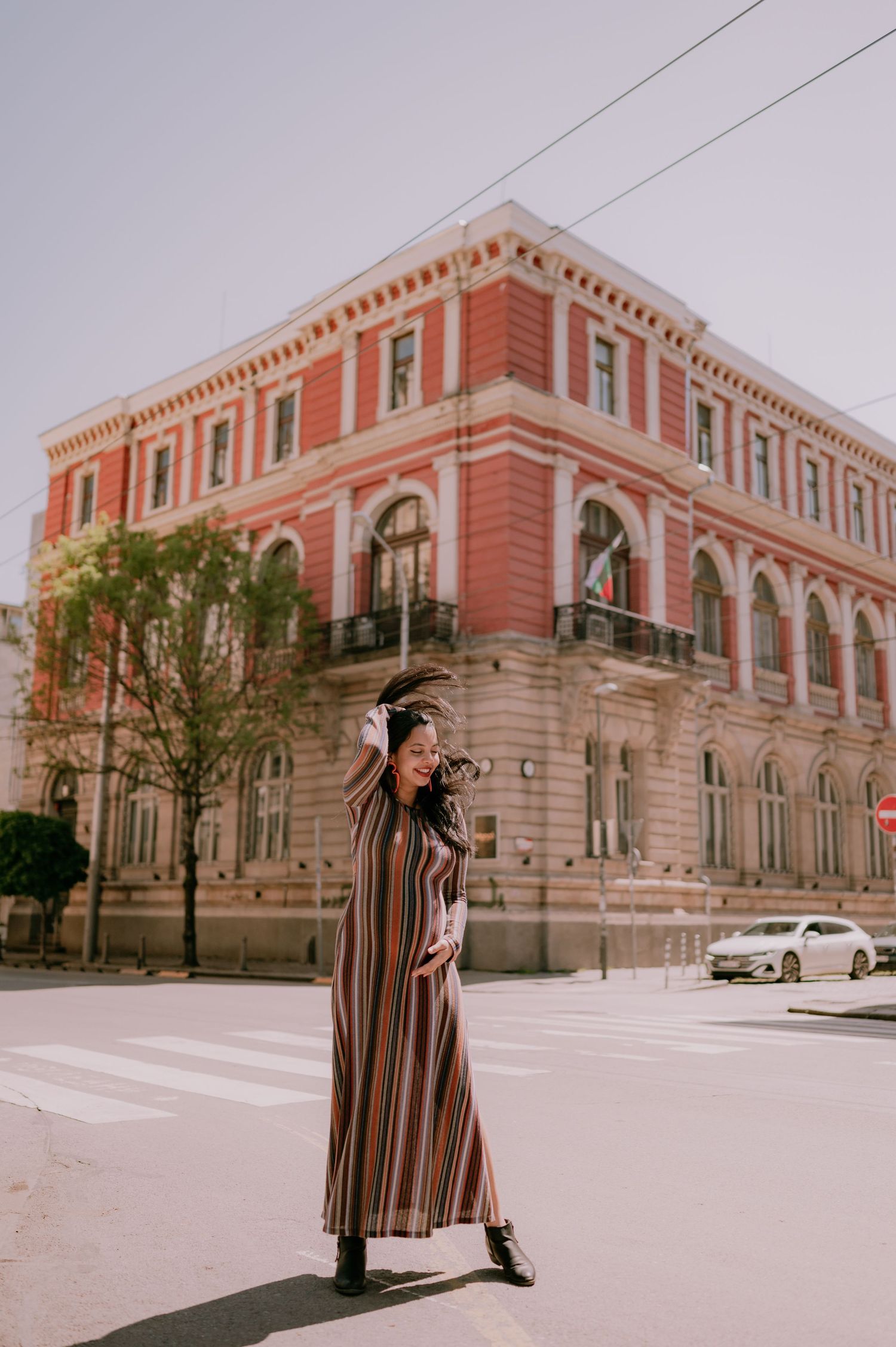 Woman in striped maxi dress posing on city street corner near historic red brick building.