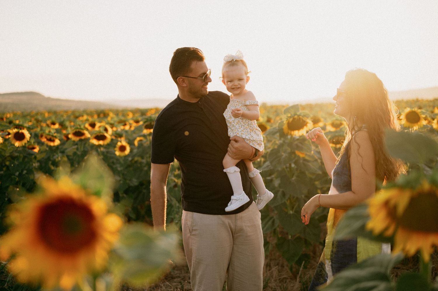 Family with baby enjoying golden hour in a sunflower field at sunset.