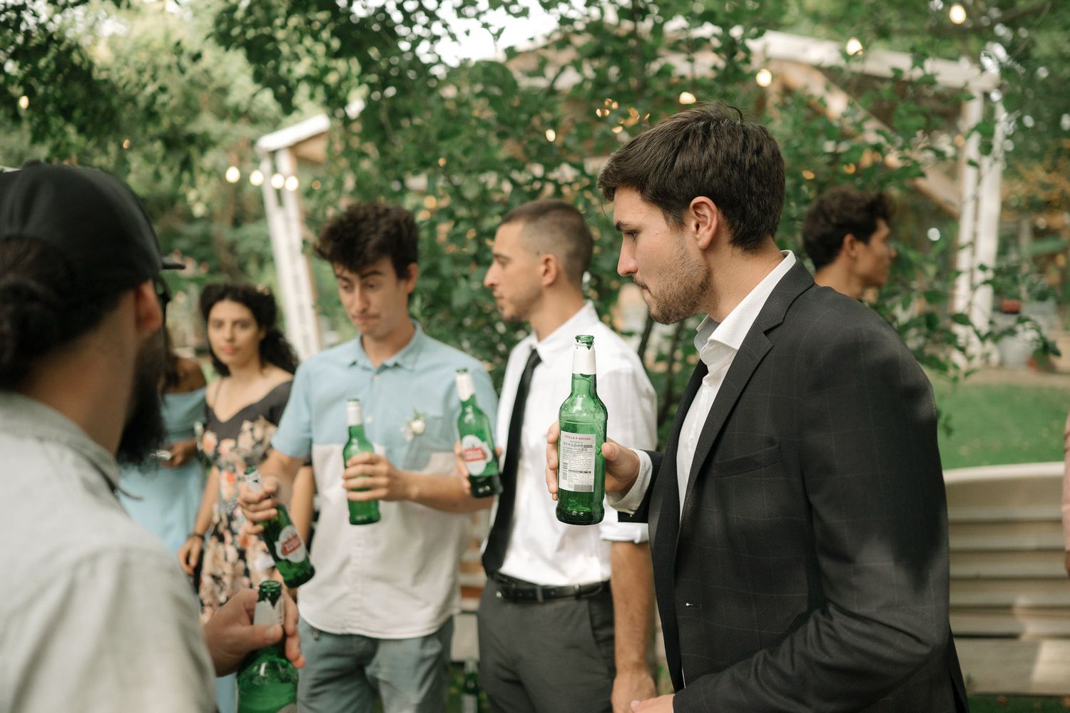A group of people standing outdoors sharing drinks and socializing at a casual gathering in a park setting.