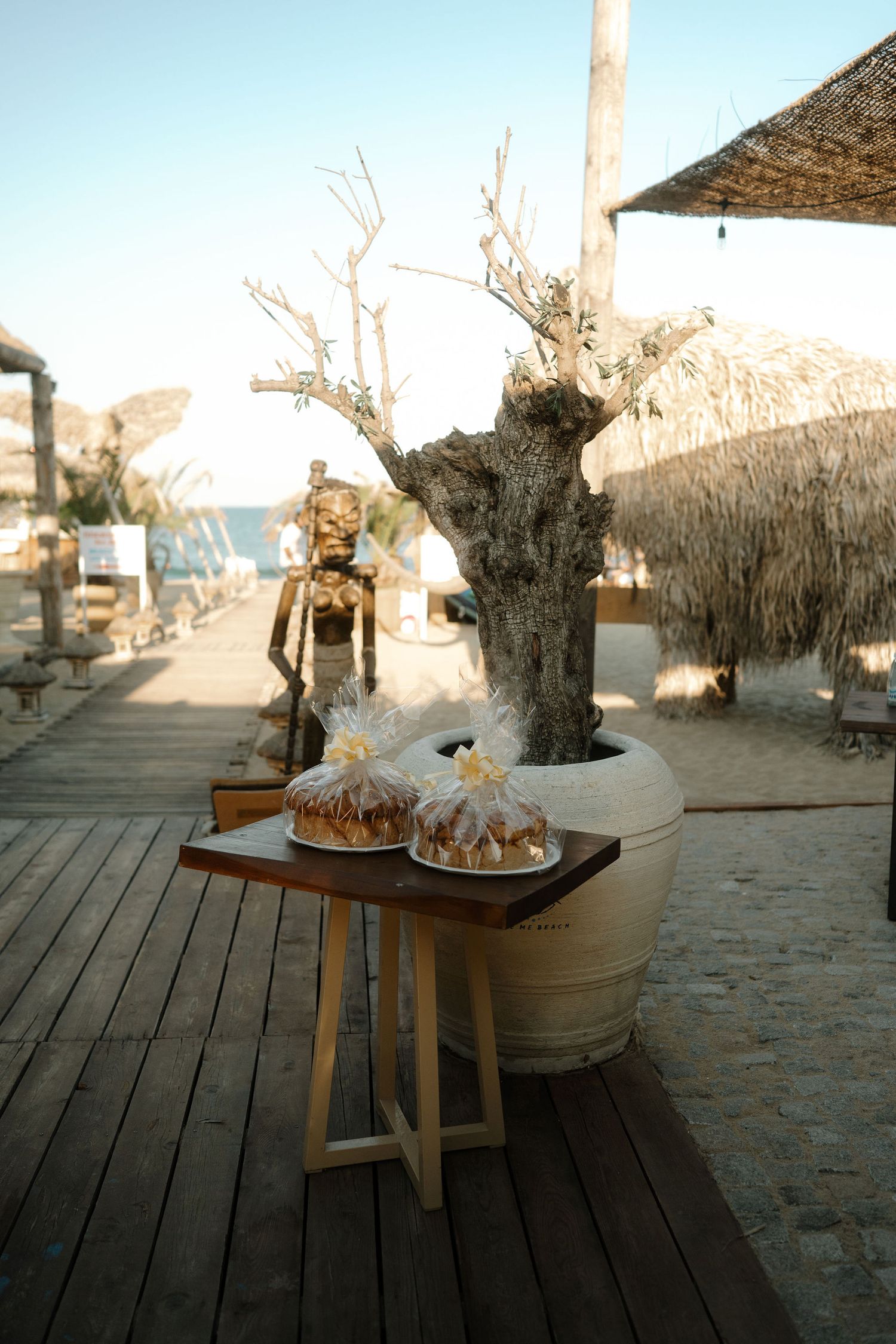 Rustic wooden deck with potted tree and decorative items at a beachside venue during sunset.