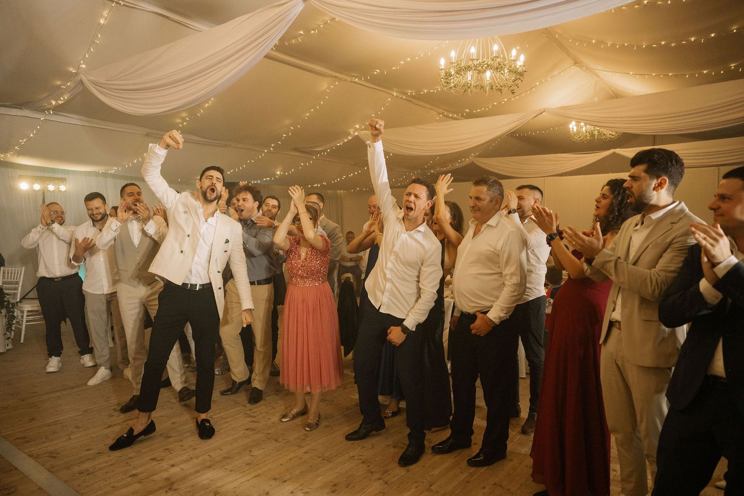 Guests celebrating joyfully on the dance floor at an elegant wedding reception with draped ceiling decor.
