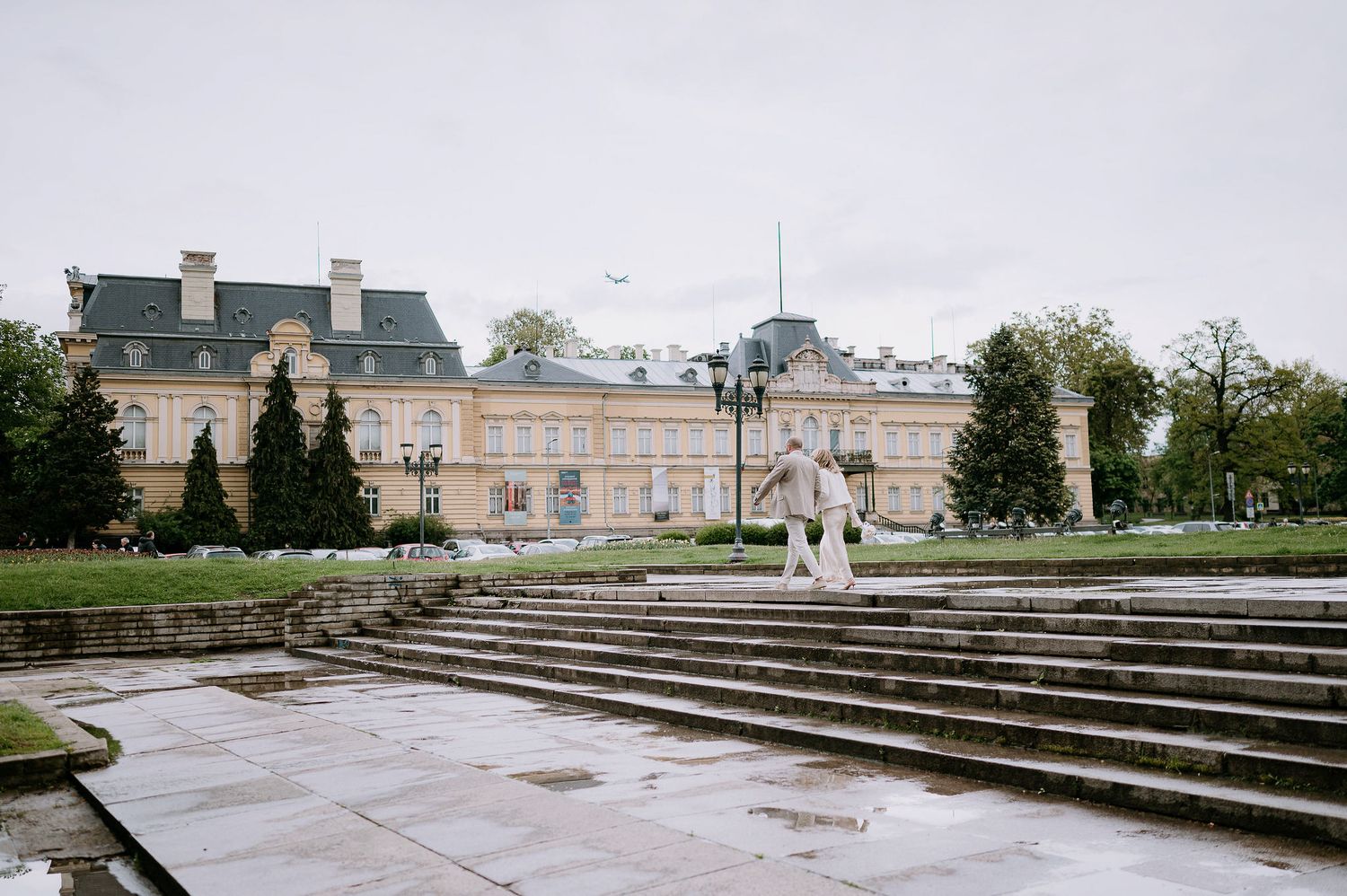 Wide stone steps lead up to a grand historic building with classical architecture and landscaping.