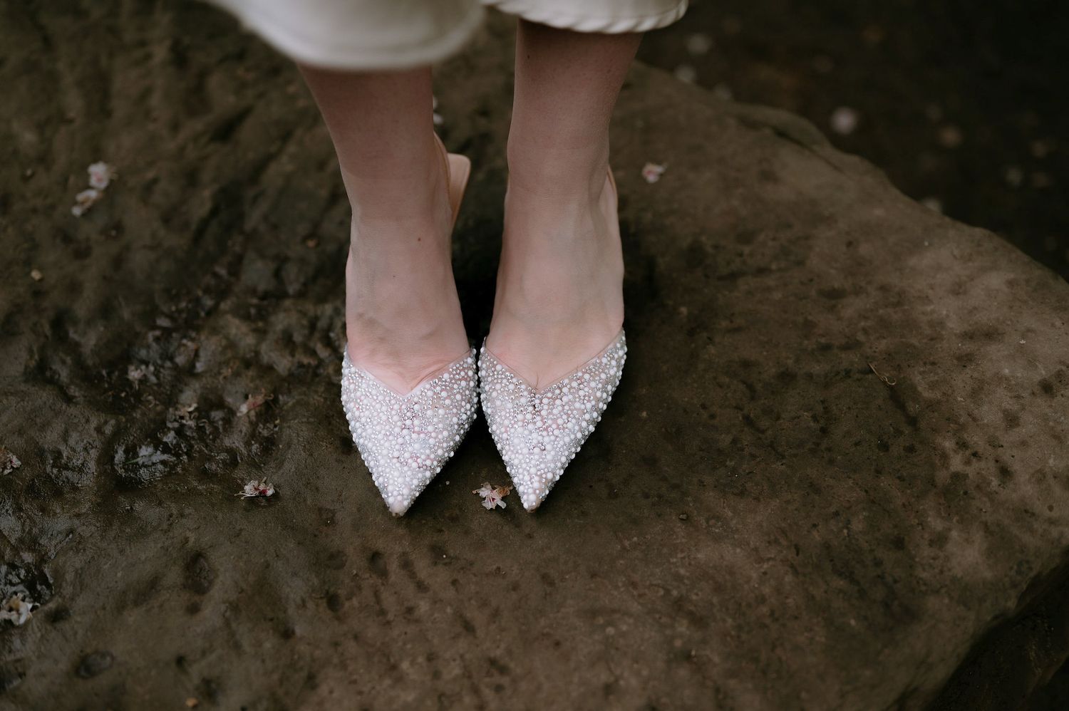 Crystal-embellished wedding shoes shown against dark stone surface.