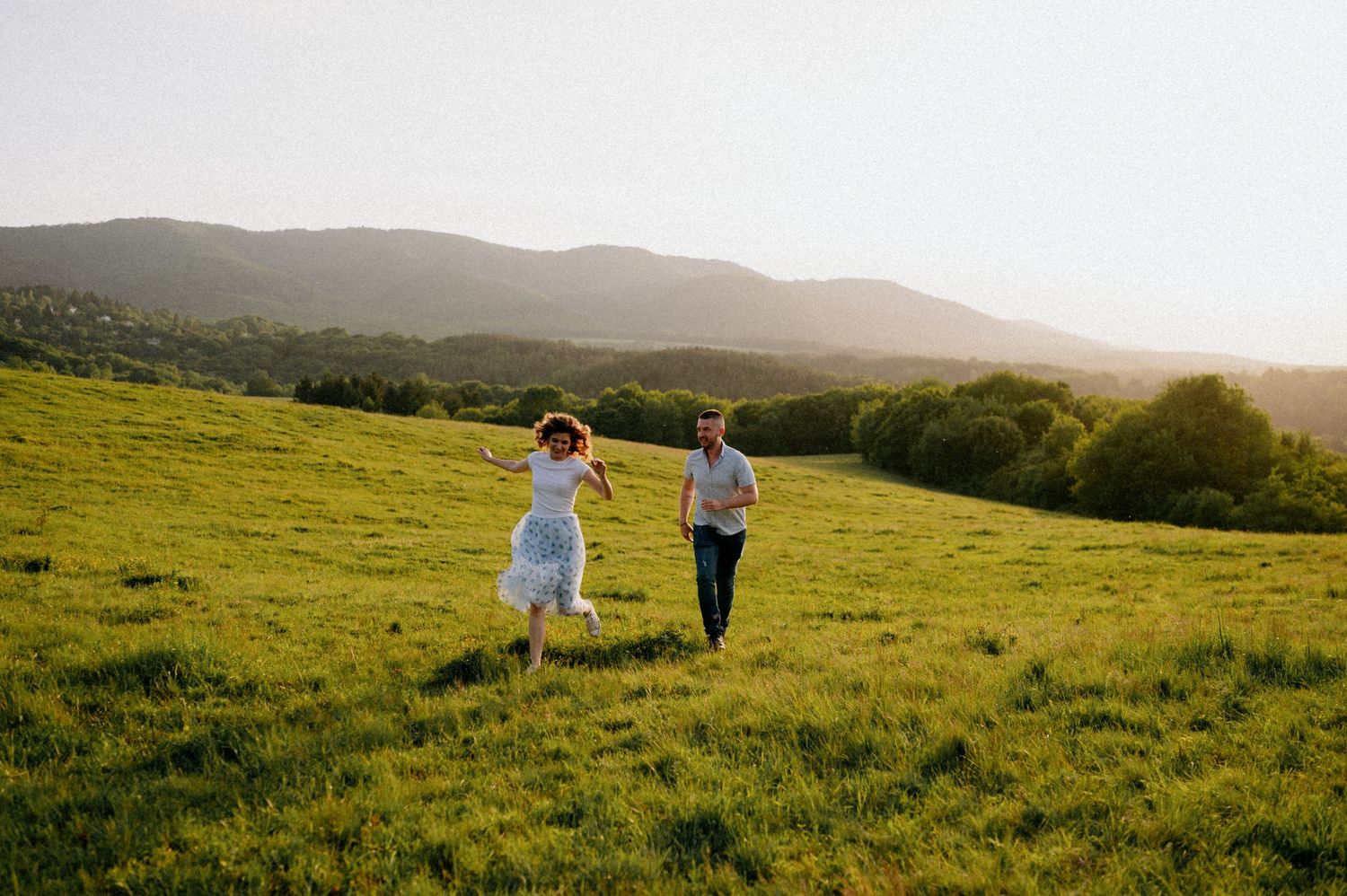 Couple running playfully through a sun-drenched hillside field.