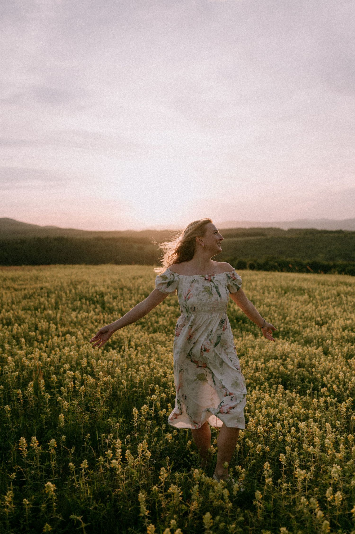 Woman in white dress twirling joyfully in a field of yellow flowers during sunset.