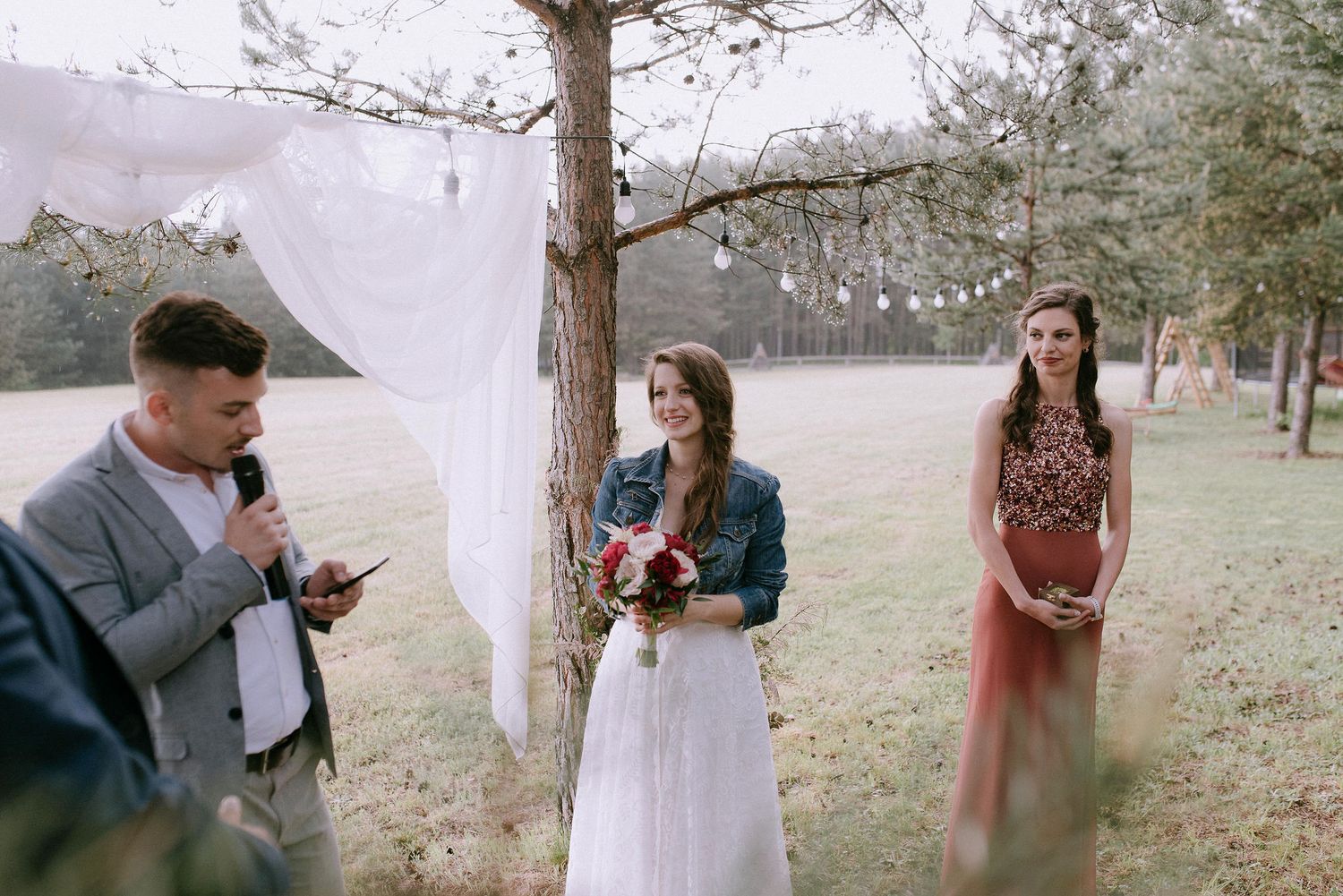 Emotional outdoor wedding ceremony moment captured beneath tall pine trees.
