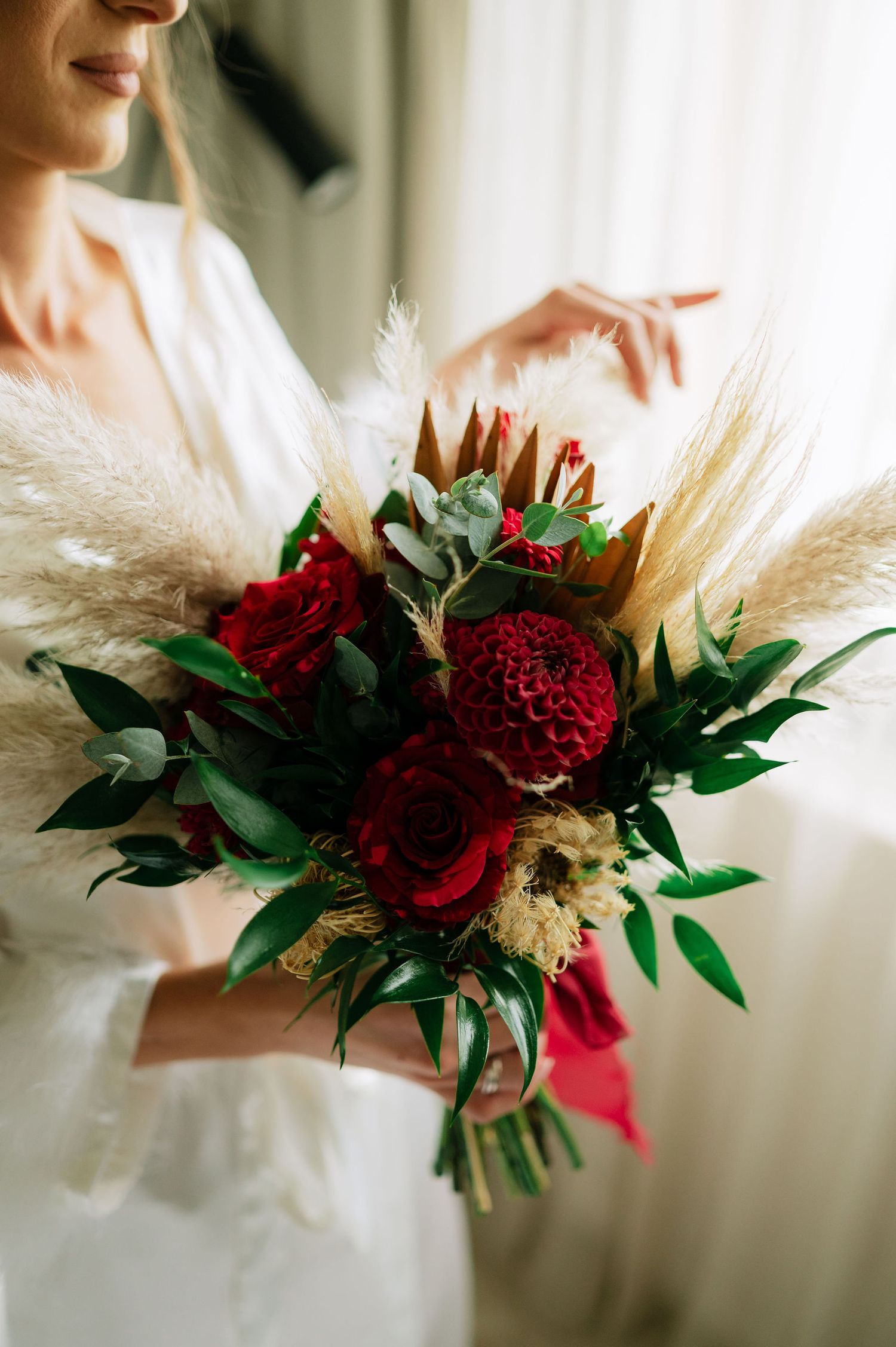 Close-up of luxurious wedding bouquet featuring deep red dahlias and pampas grass.