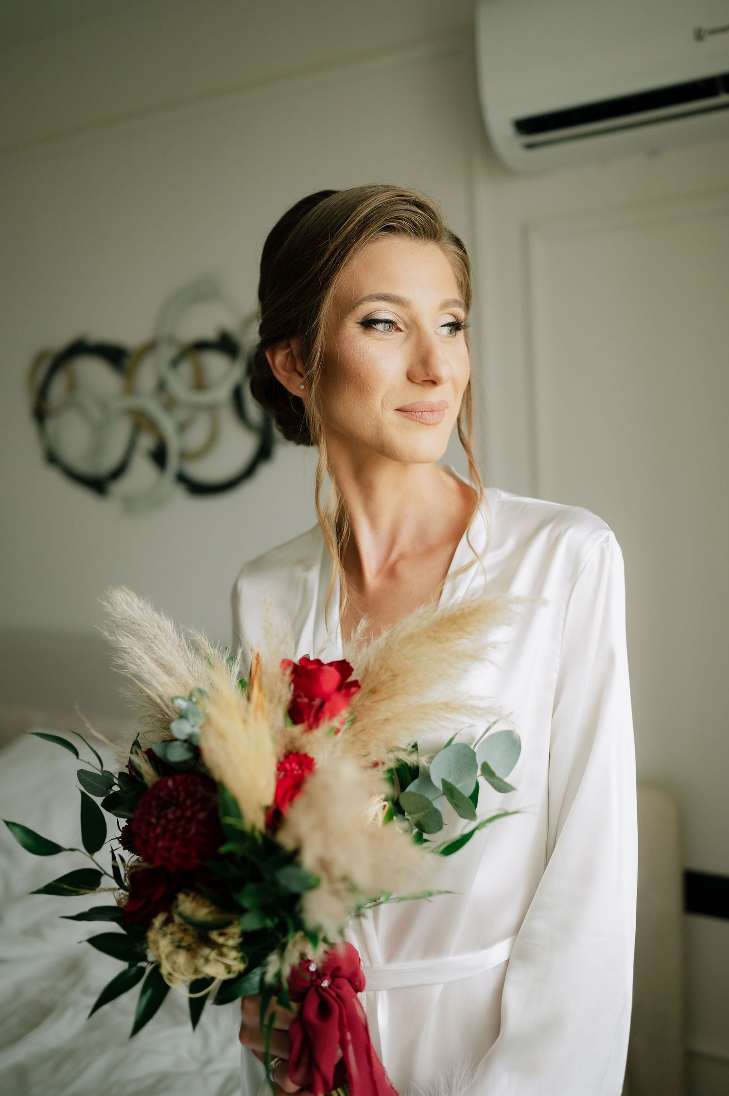 Beautiful bridal bouquet with red flowers and pampas grass held against a white robe.