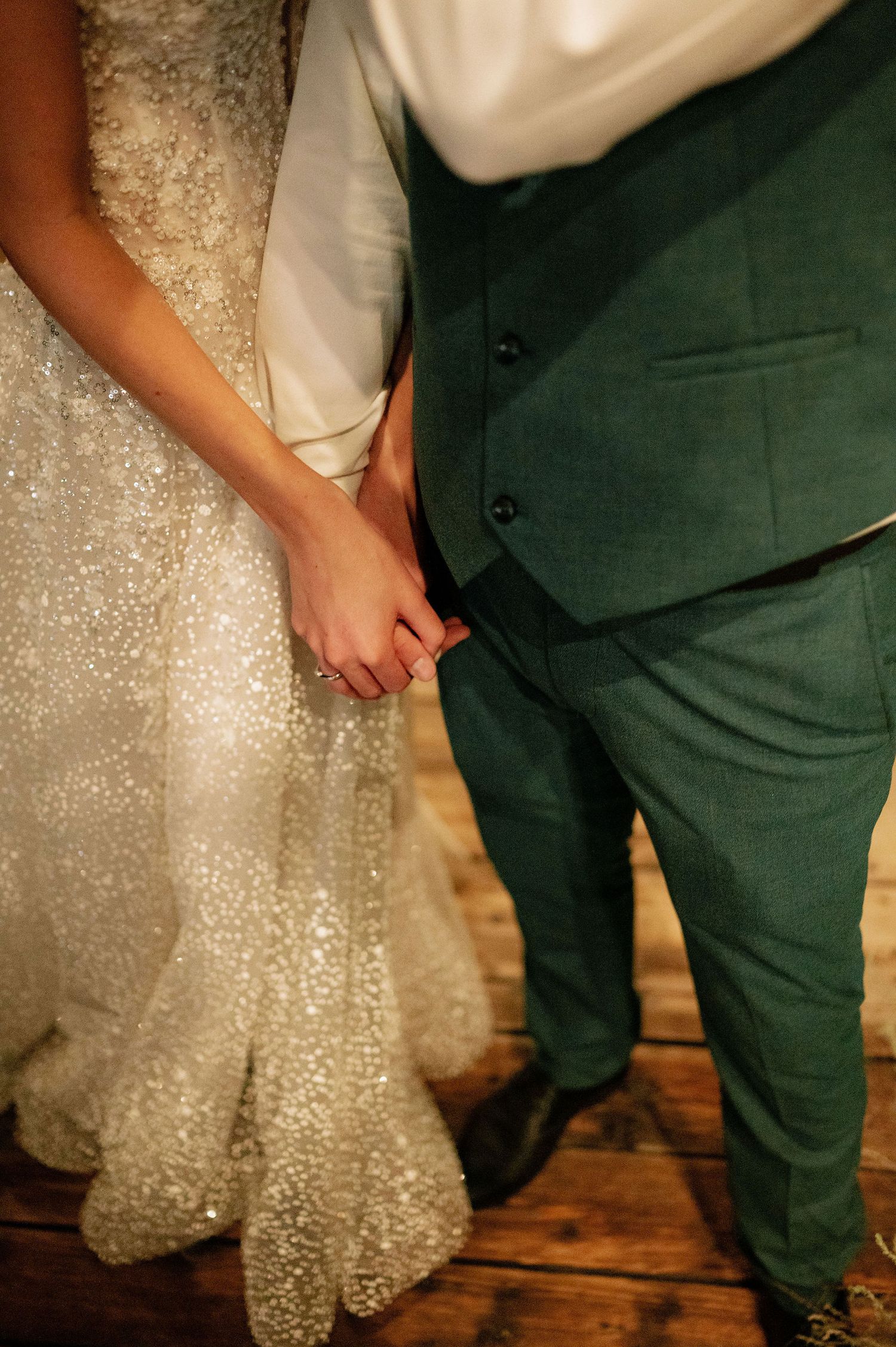 Close-up details of a sparkly white wedding dress and dark suit at an elegant wedding ceremony.