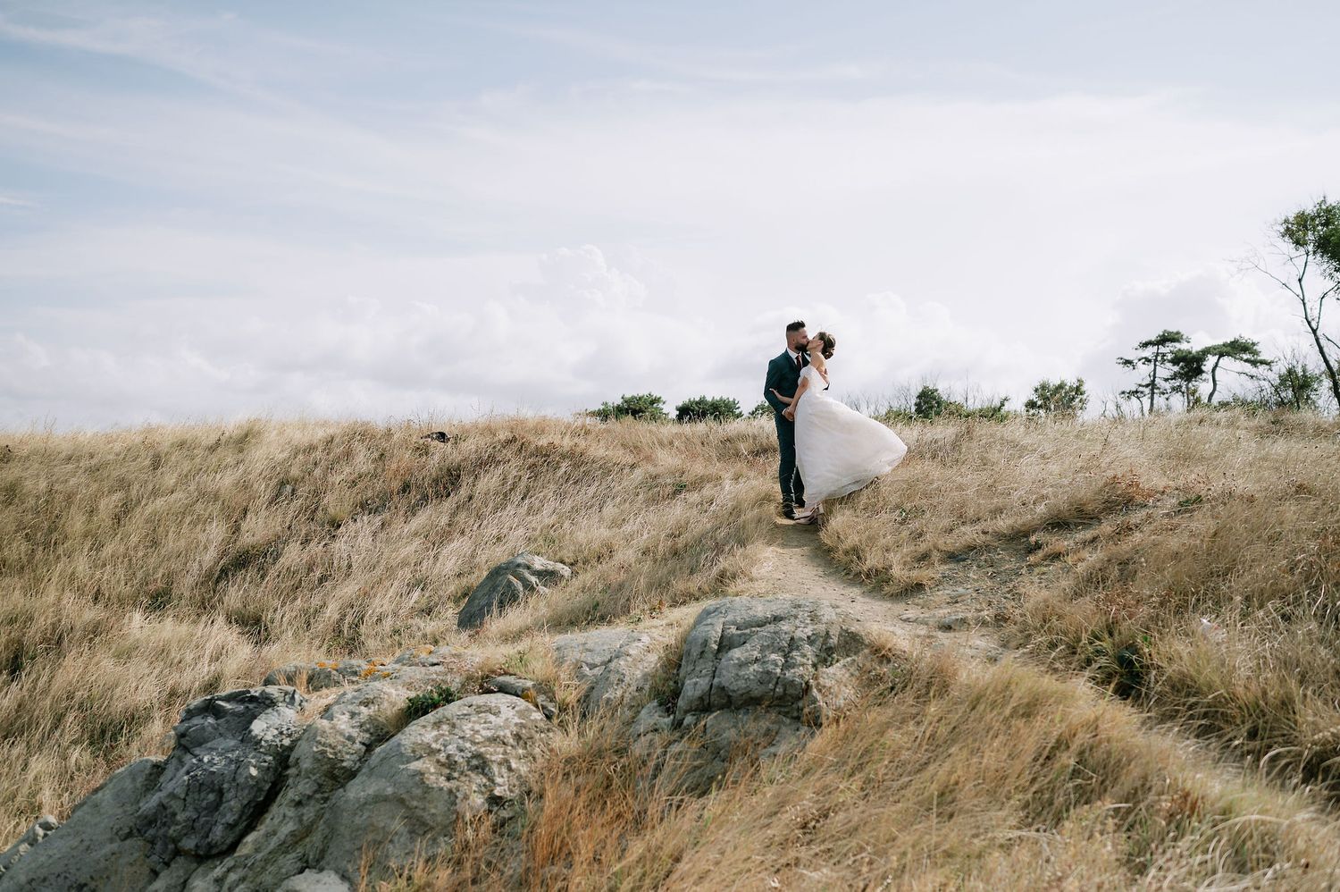 Wedding couple explores rugged coastal terrain with dramatic ocean views in background.