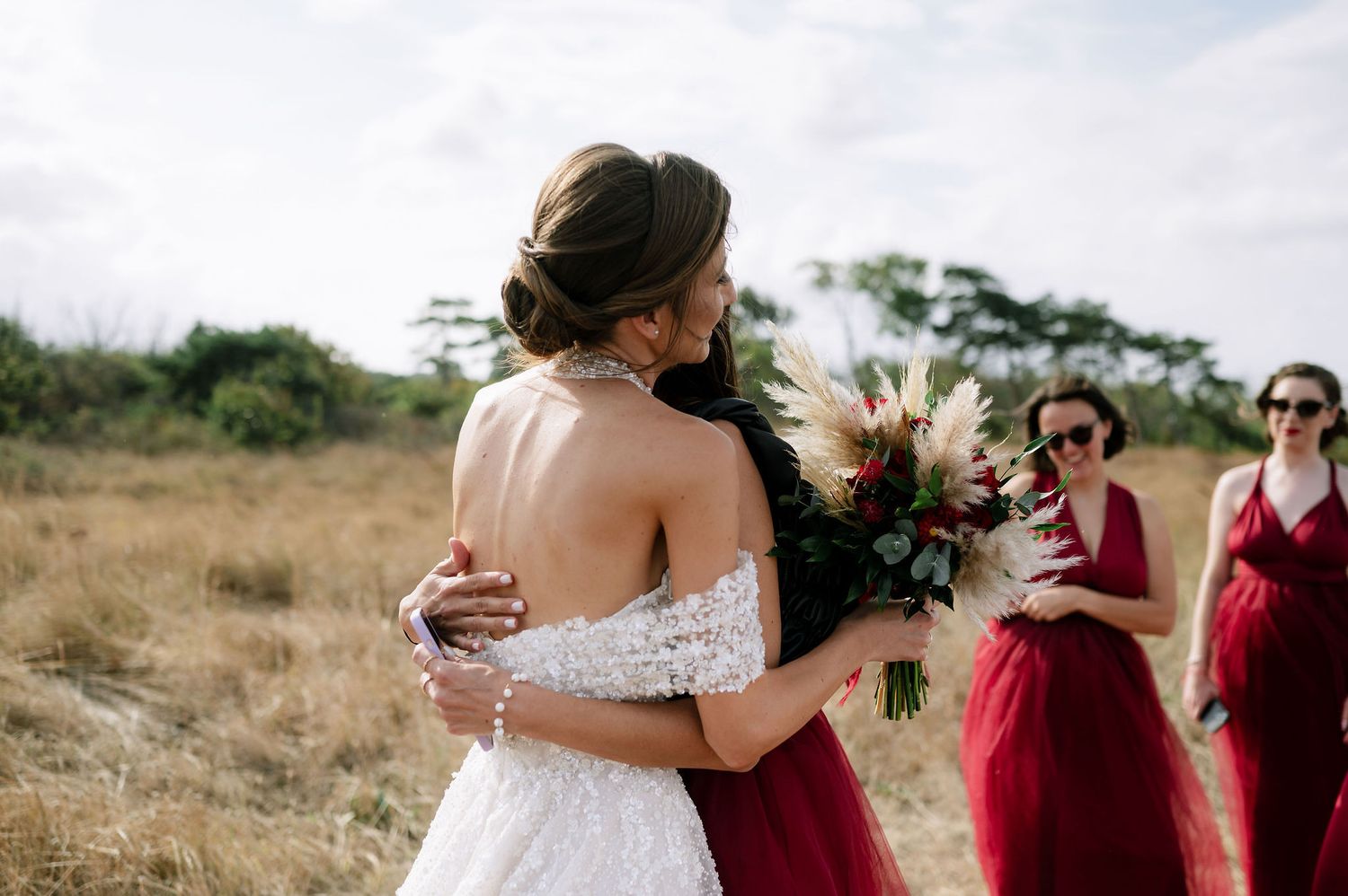 Wedding party members share a joyful moment outdoors in burgundy and white attire.