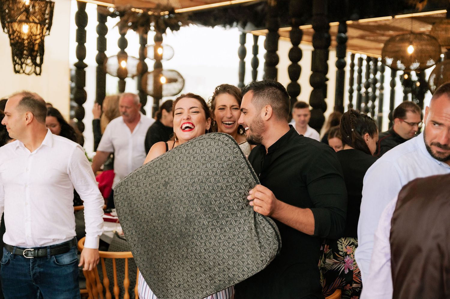 Wedding guests sharing a joyful moment with grey blanket at indoor reception.