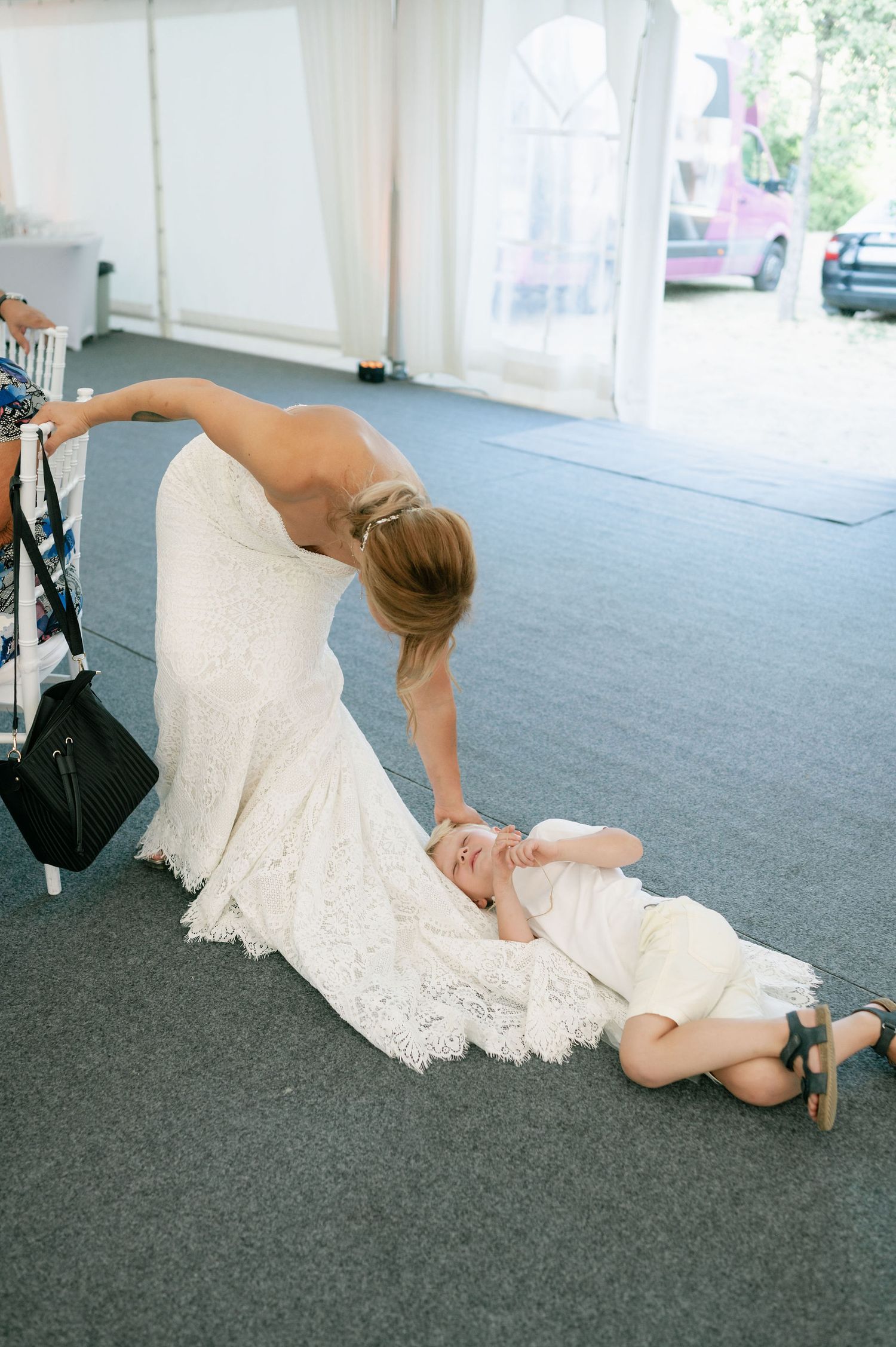 A person in a white lace dress lying dramatically on gray carpet.