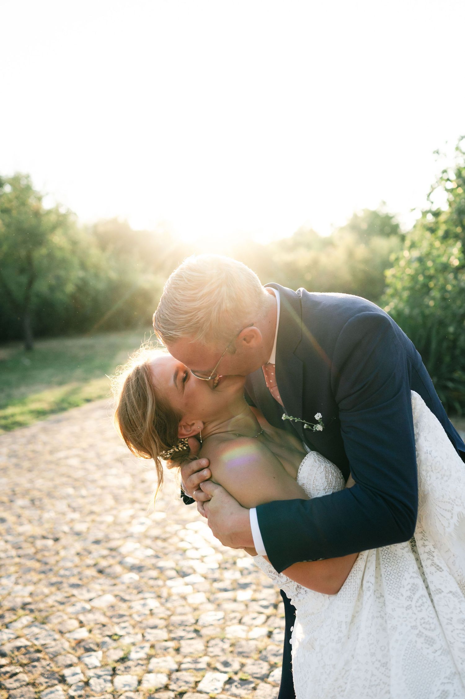 A romantic dip kiss between newlyweds on a cobblestone path at sunset.