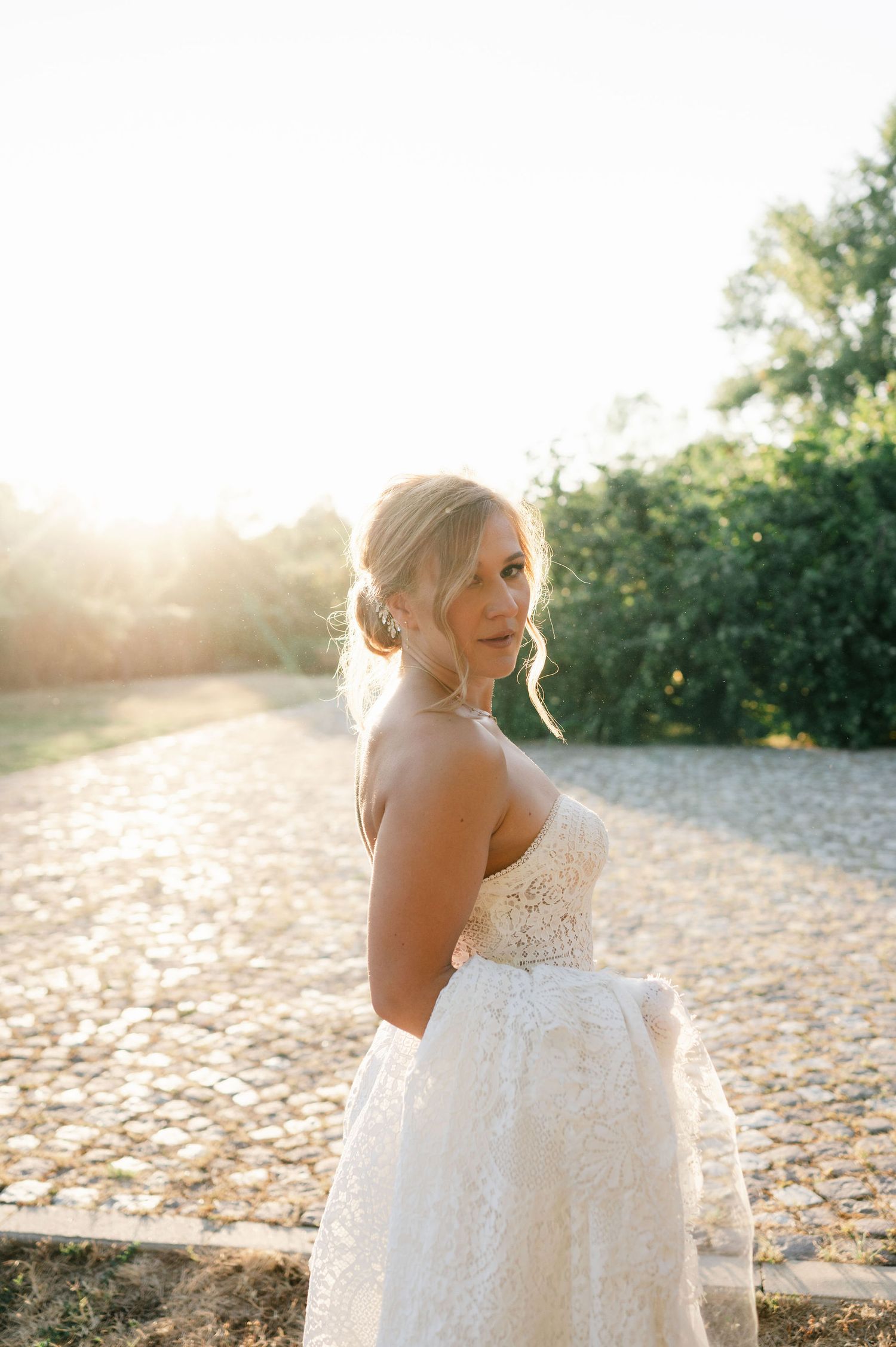 Bride in strapless lace wedding dress poses during golden hour photography session.