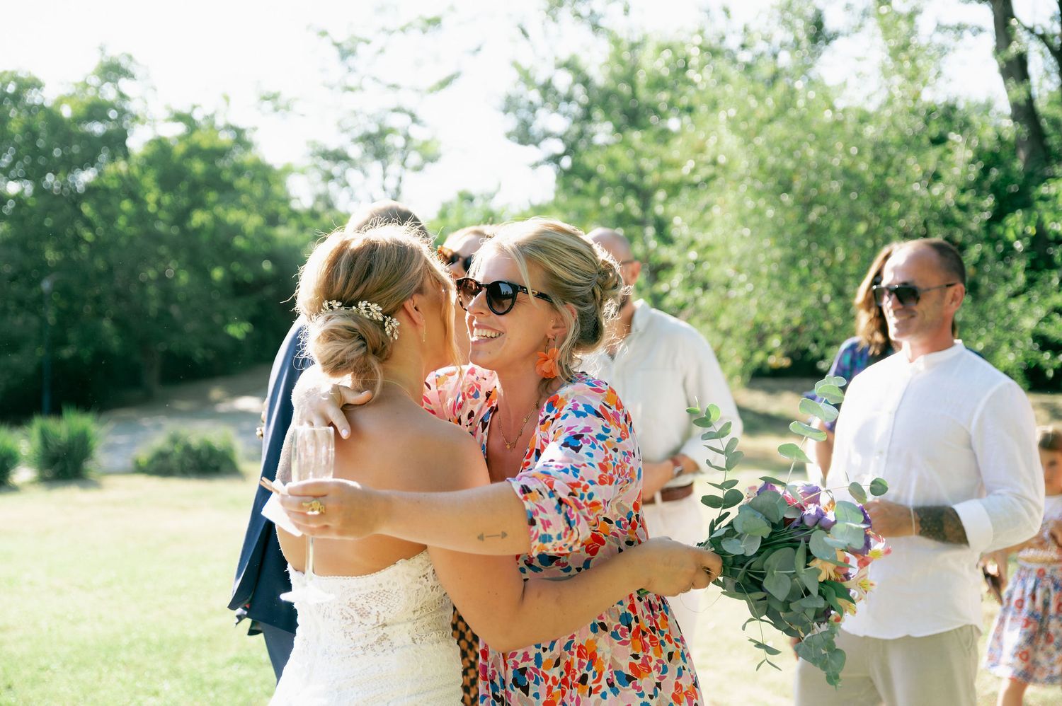 Wedding party members share laughs and embraces during an outdoor summer celebration.