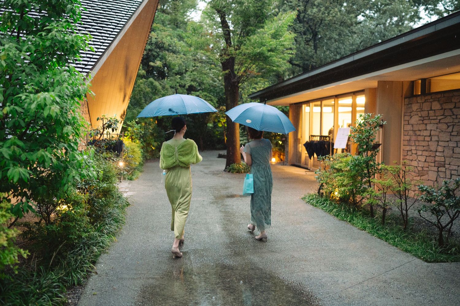 A peaceful garden walkway lit by lanterns leads to a traditional Japanese-style building at twilight.