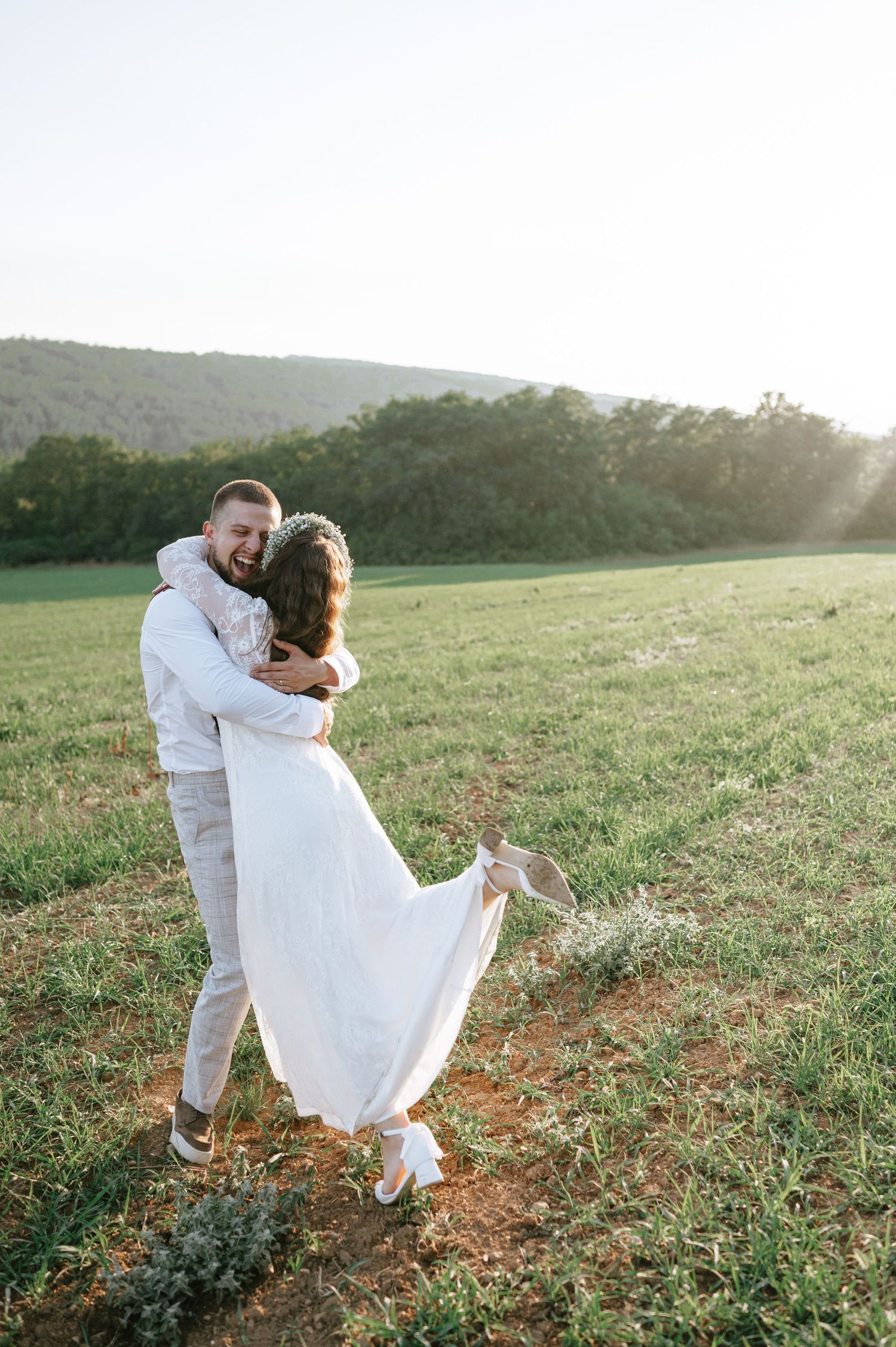 Newlyweds dance playfully in a sunlit meadow during golden hour.