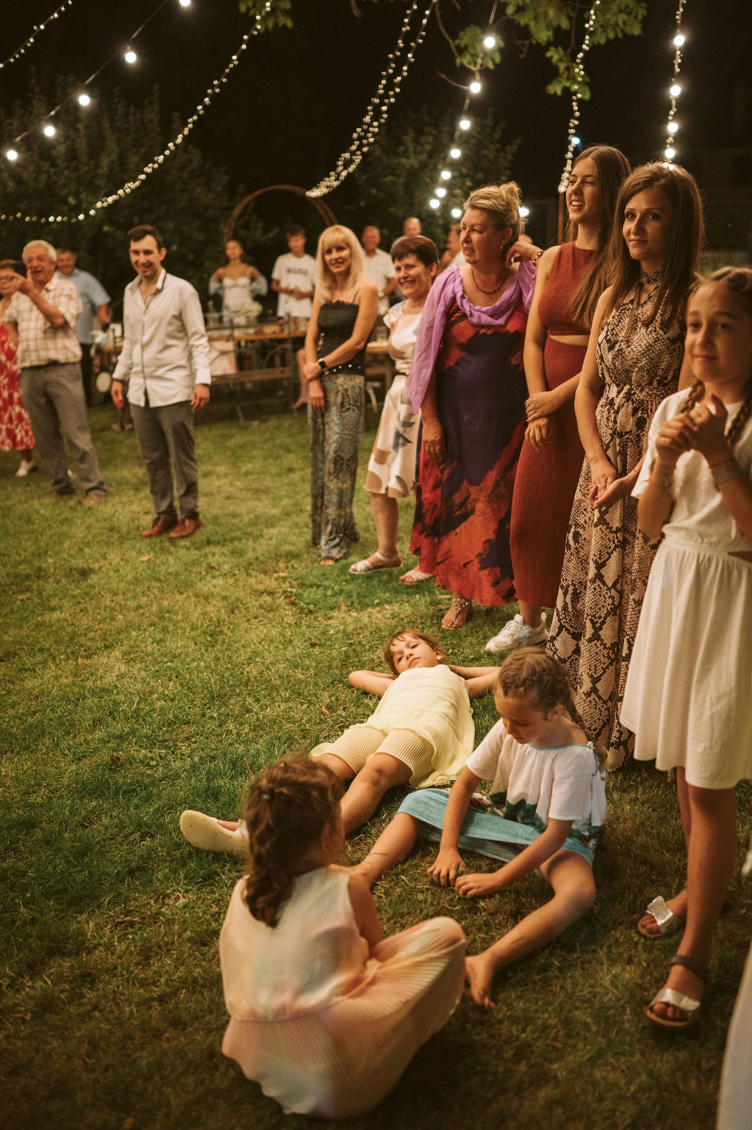 Wedding guests dancing and having fun under string lights at an outdoor reception.
