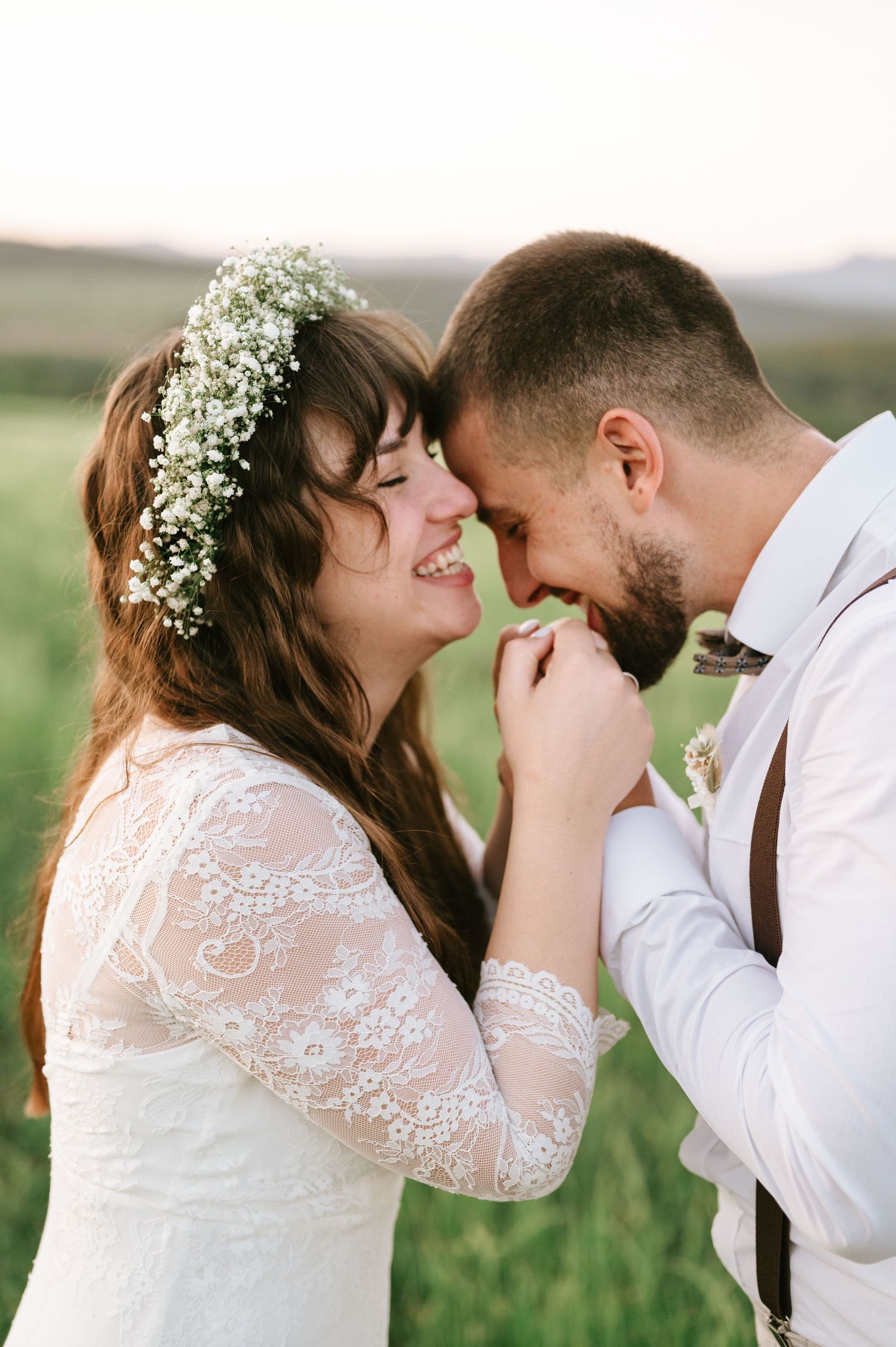 A romantic wedding portrait shows tender moments between newlyweds in a grassy field.