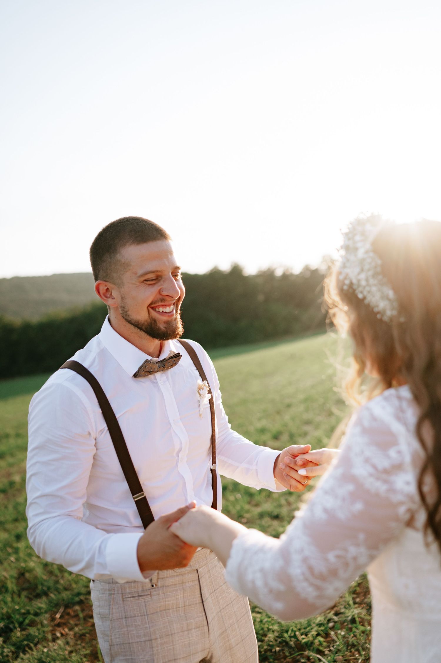 A joyful moment between newlyweds laughing together in a sunlit field.