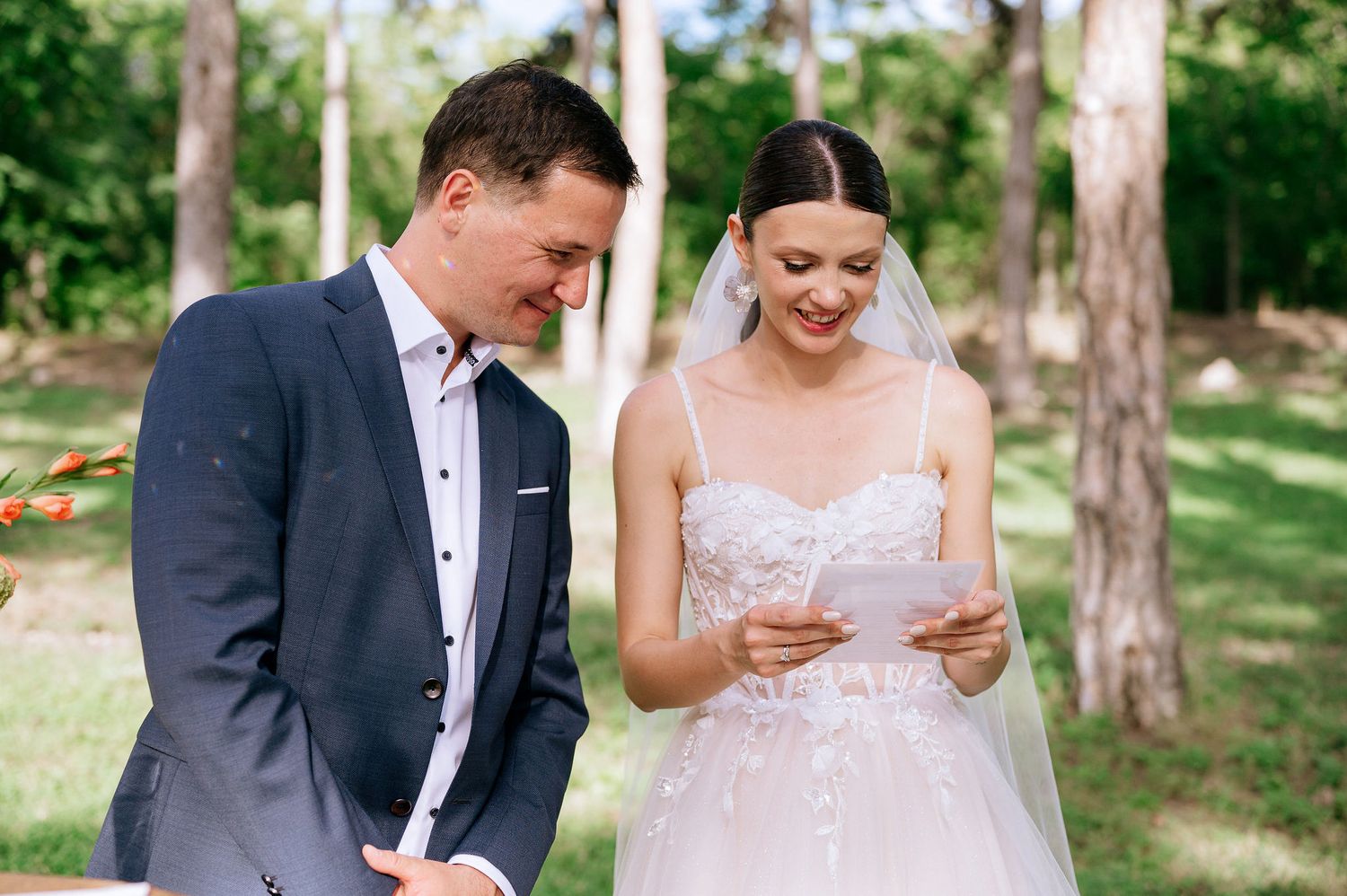 Elegant outdoor wedding scene with couple among pine trees and white floral arrangements.