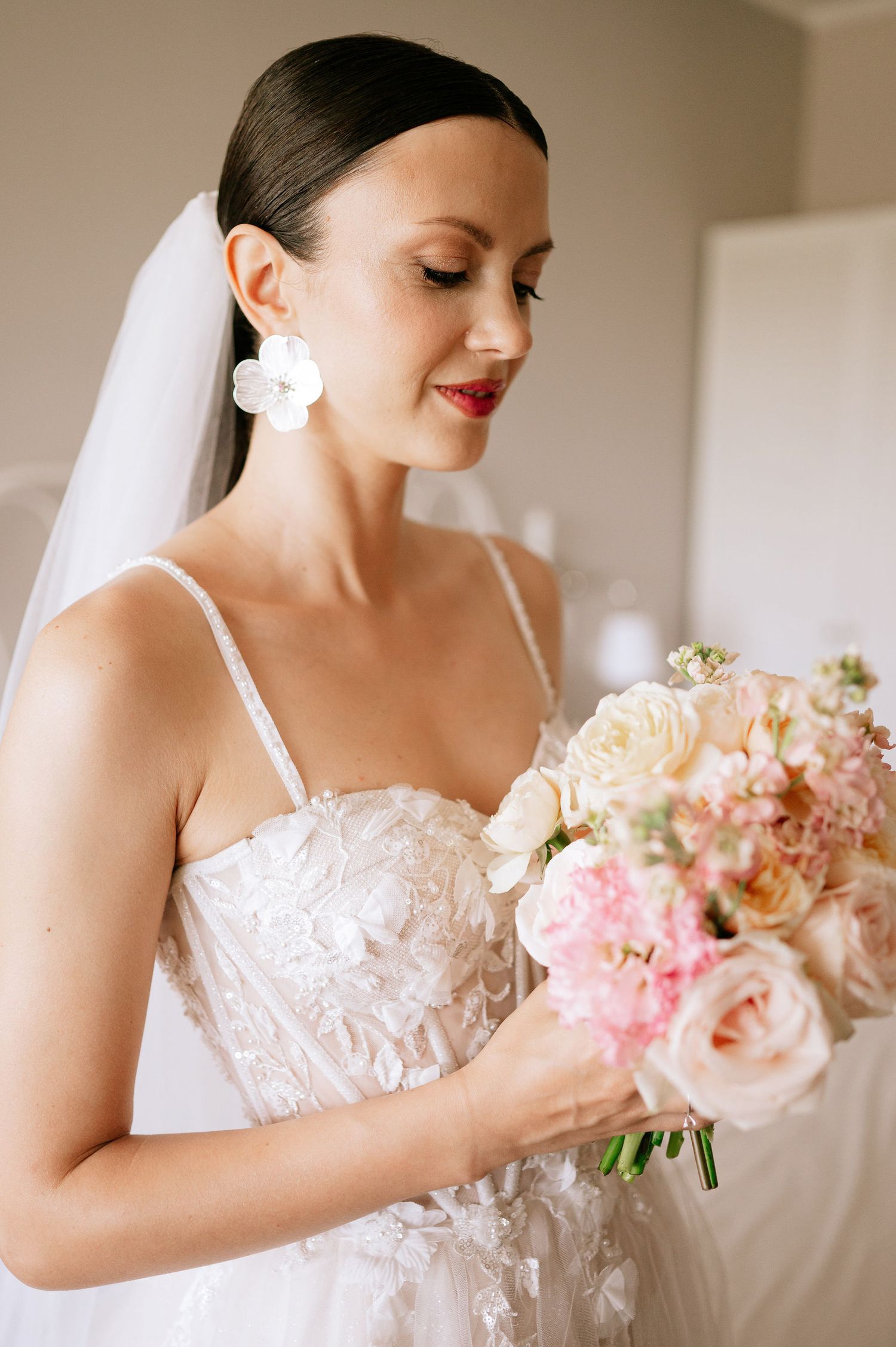 Bride admiring her romantic pink and peach floral bouquet in natural light.
