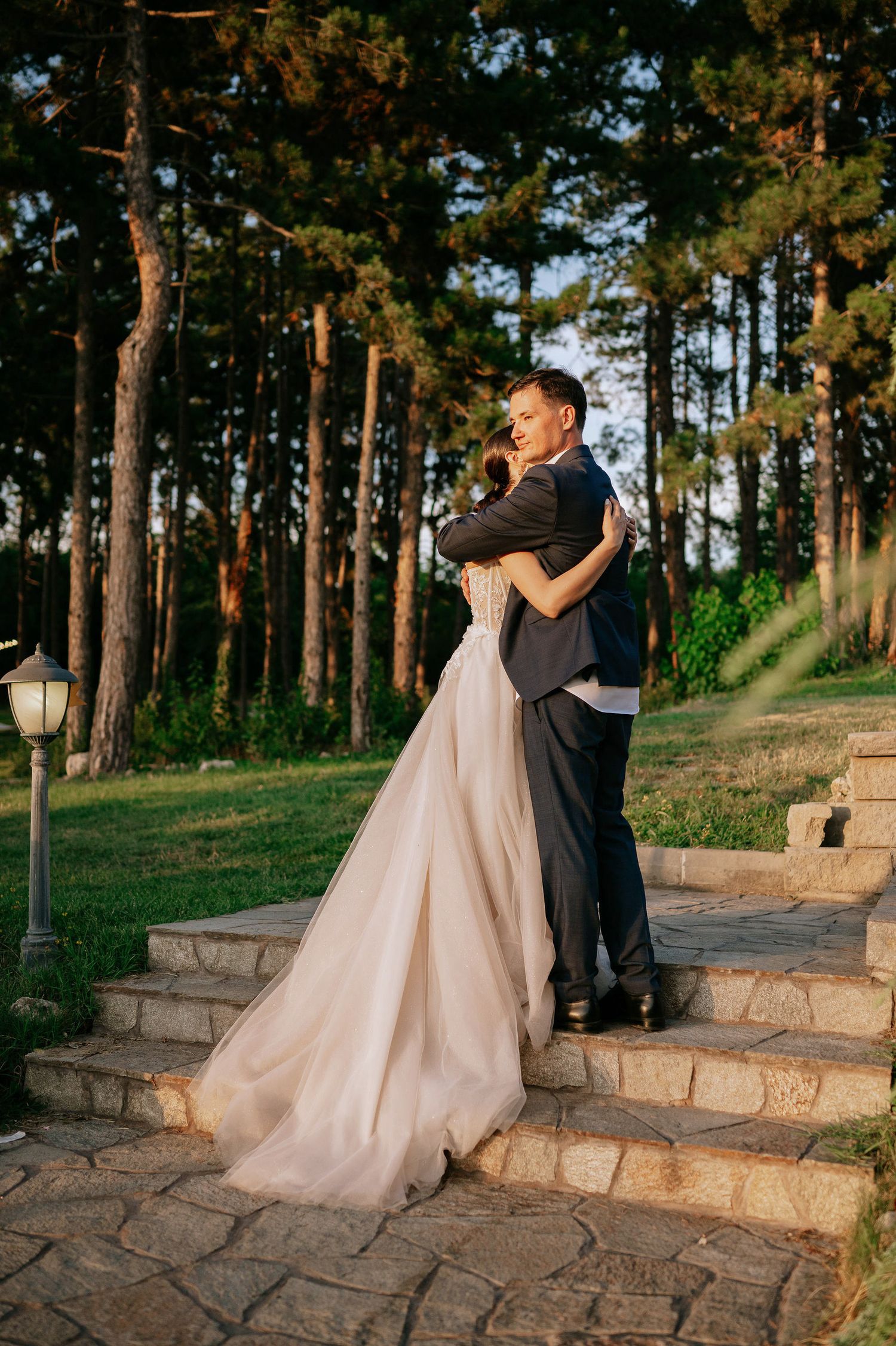 Wedding couple dancing together on stone steps surrounded by pine trees.