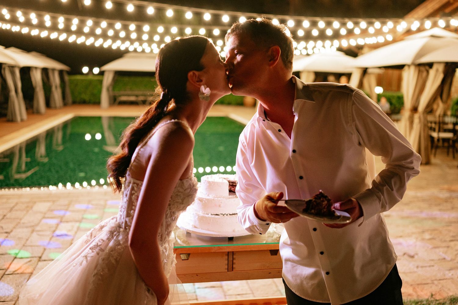 Guests gather under string lights at an outdoor wedding reception venue.