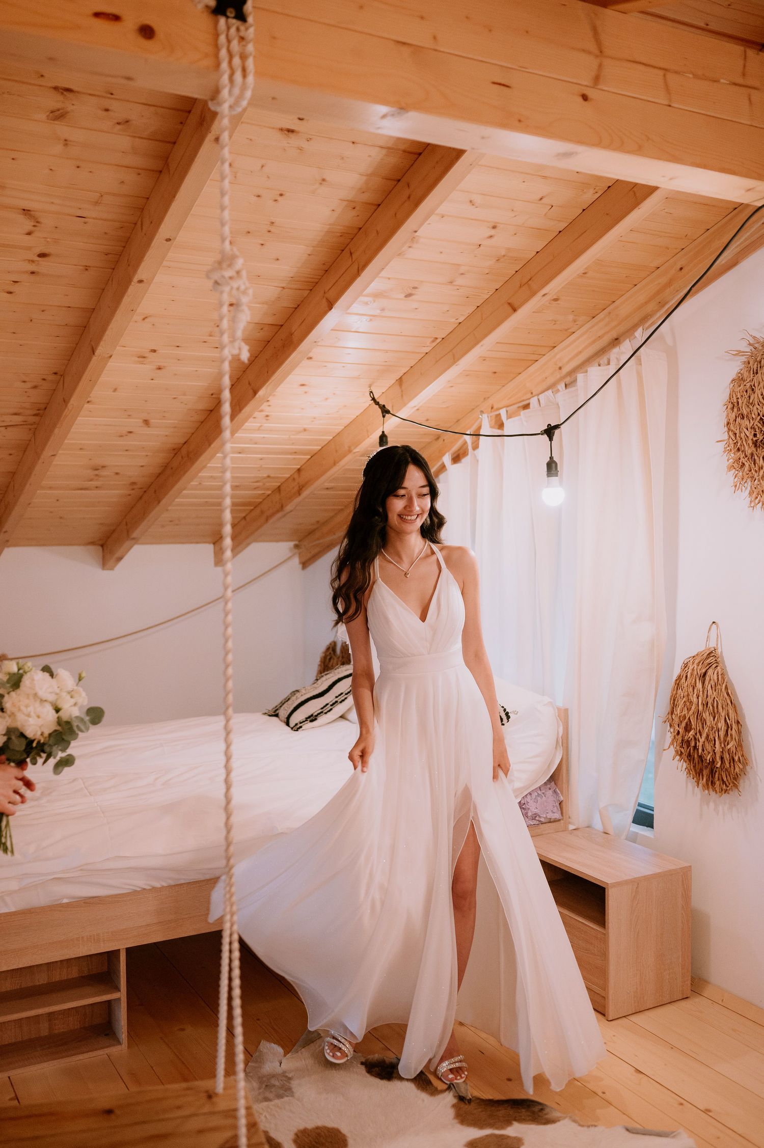 Ethereal bridal portrait in flowing white dress against rustic wooden beams and white curtains.