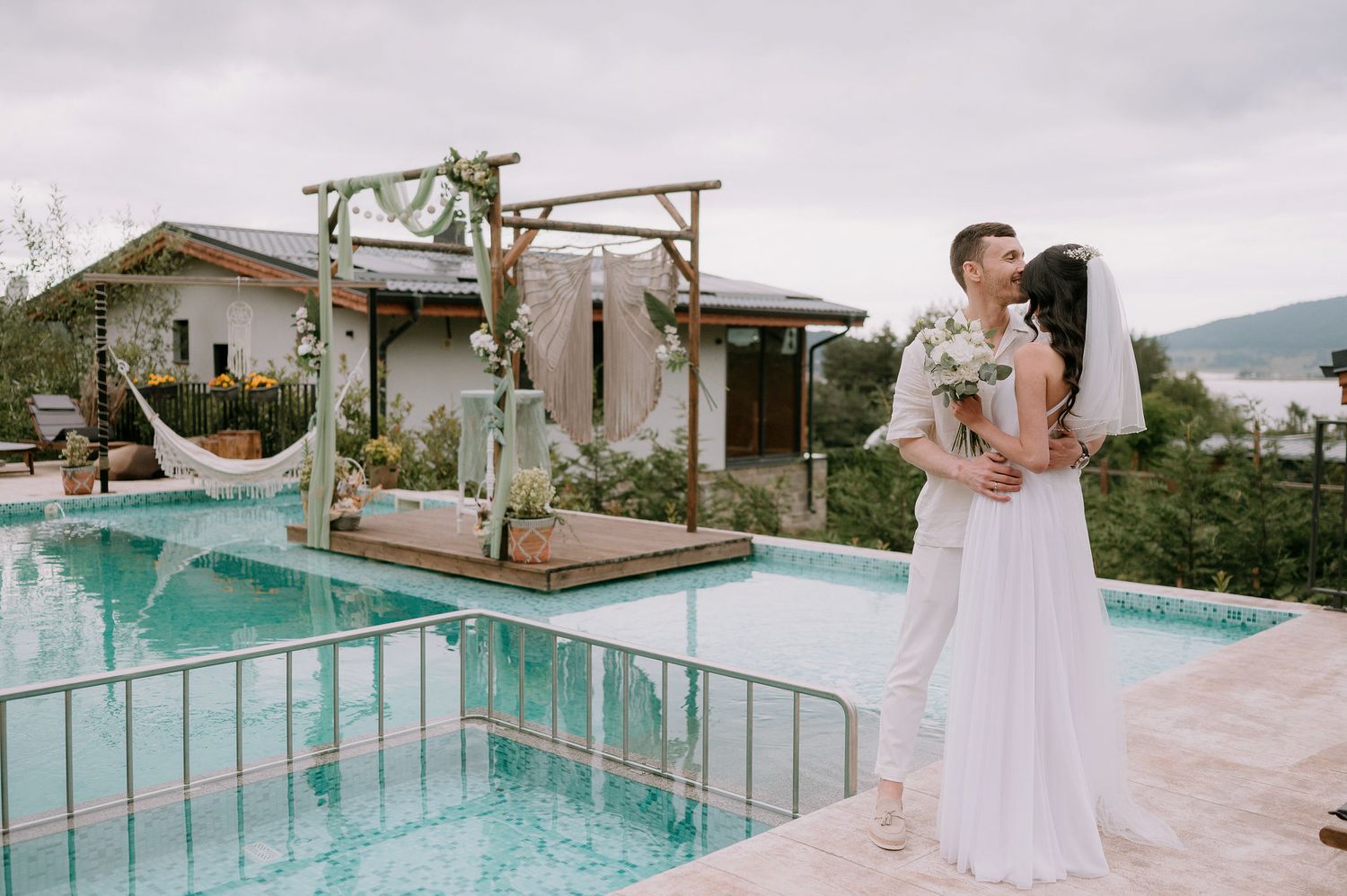 Intimate wedding ceremony setup near a glass-railed pool with mountain landscape views.