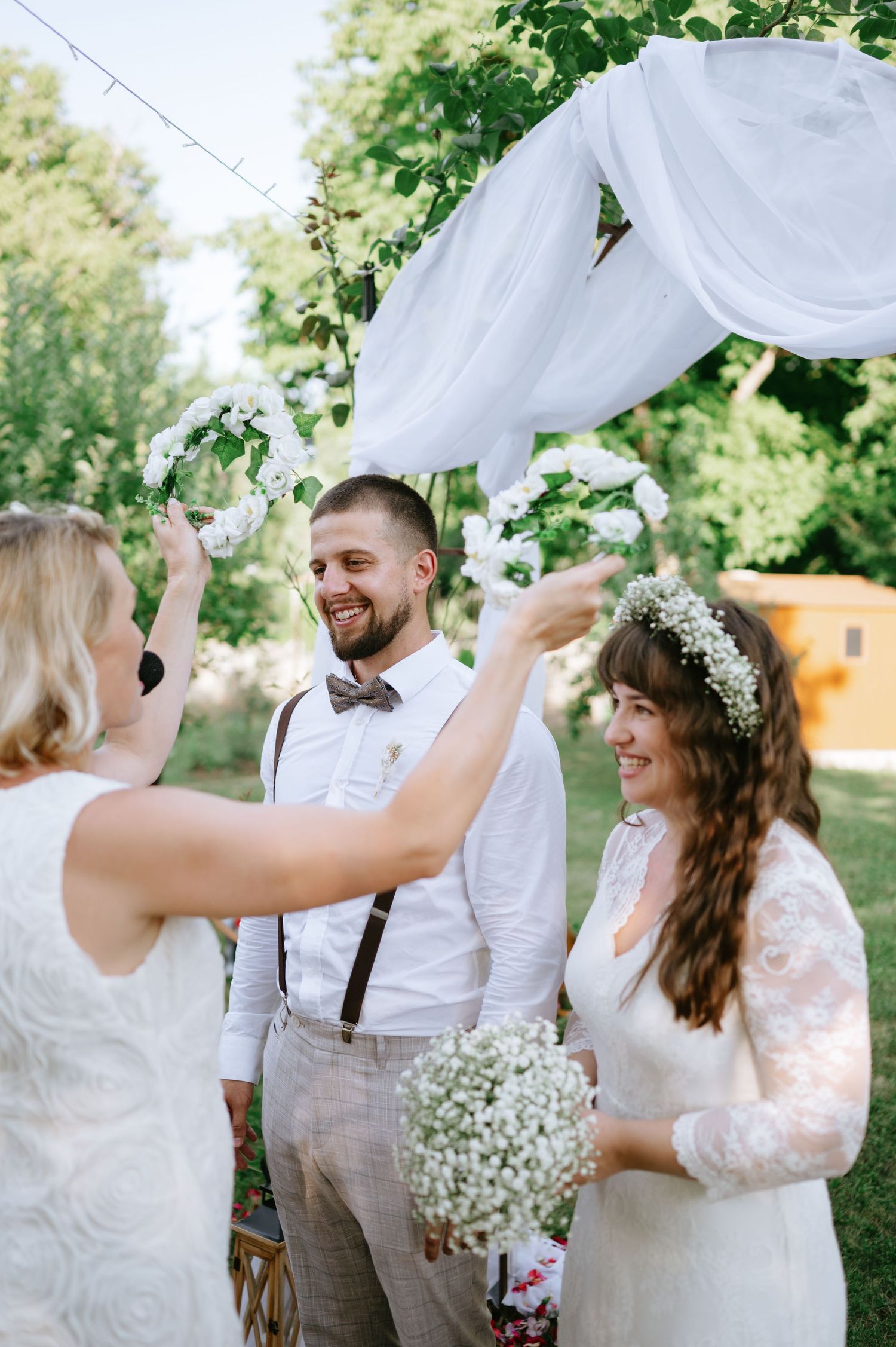 A joyous wedding celebration moment under a white draped arch in a garden setting.