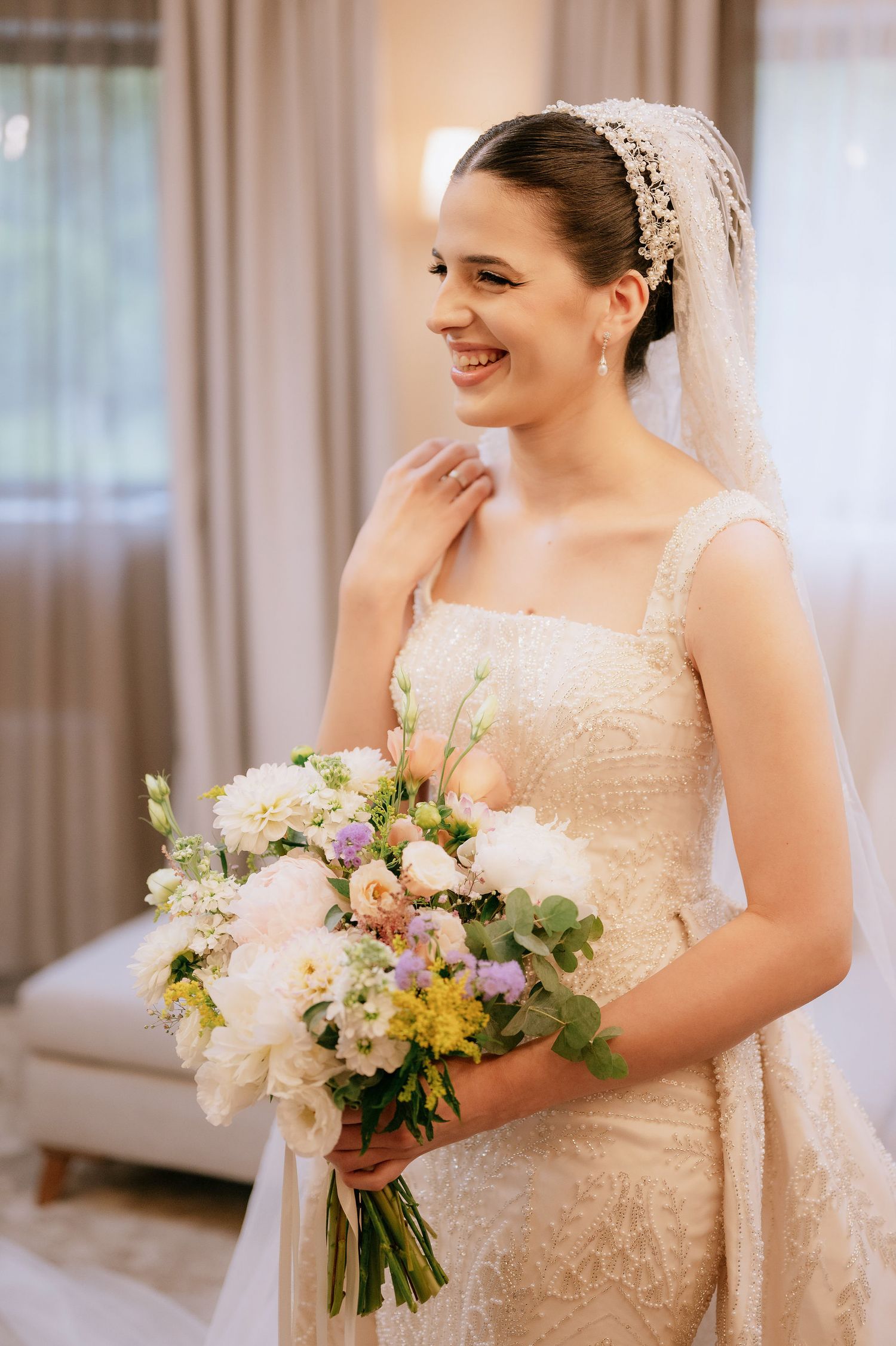 Joyful bride smiling while holding elegant bouquet of mixed spring flowers.