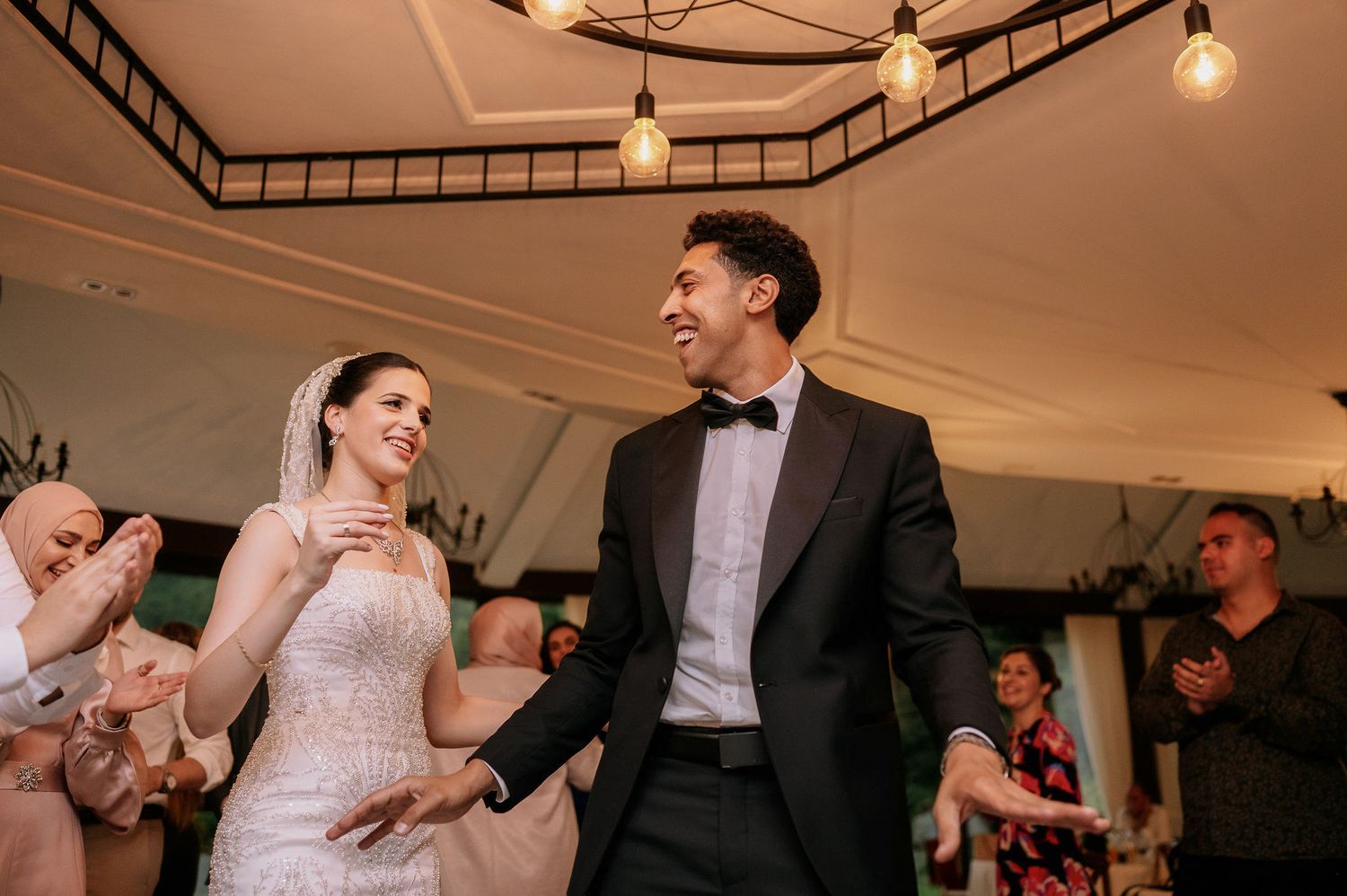 Wedding reception venue decorated with hanging string lights and dark wooden beams.