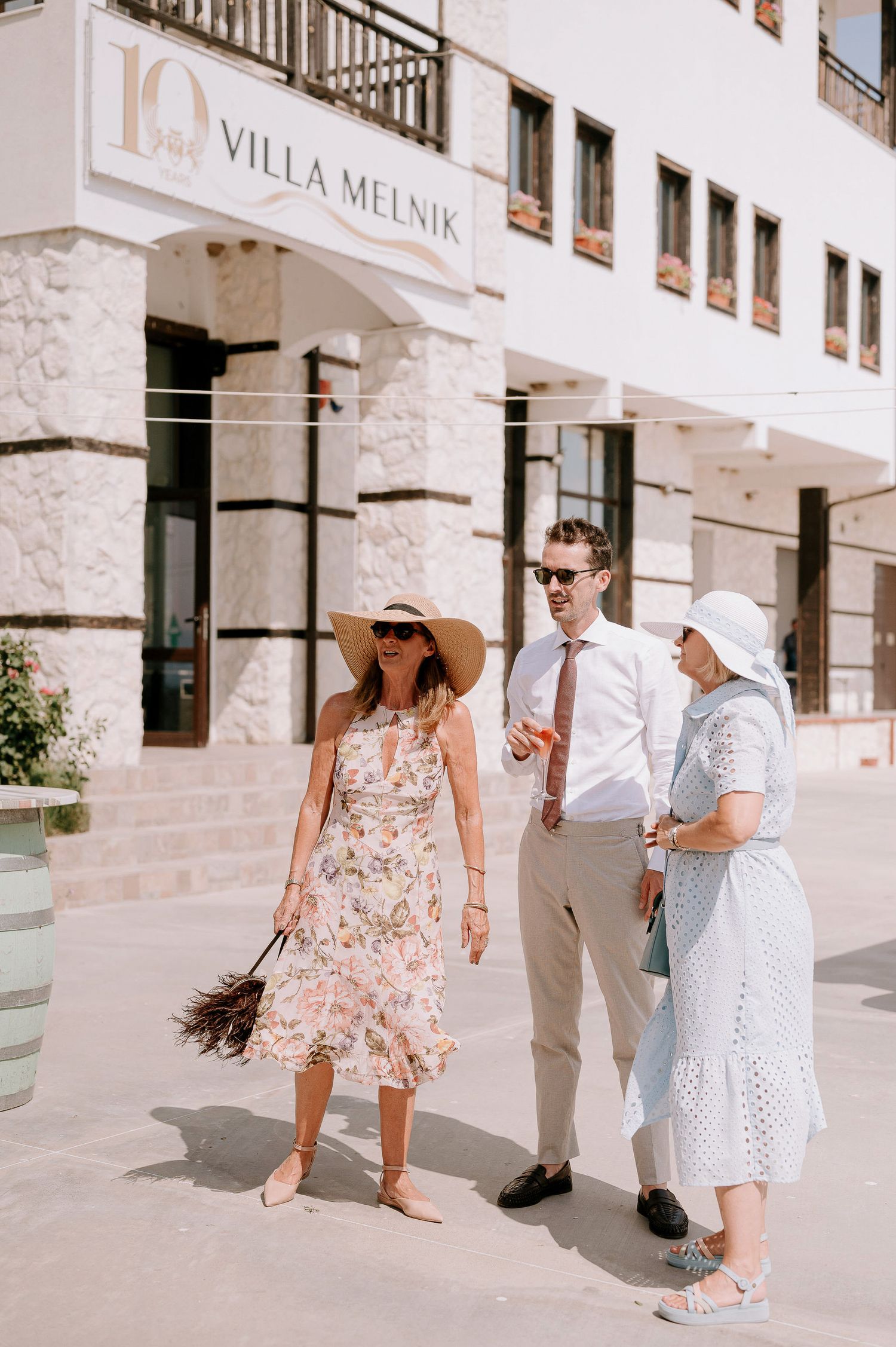 Group gathering outside Villa Melnik's entrance in light summer clothing and sun hats.