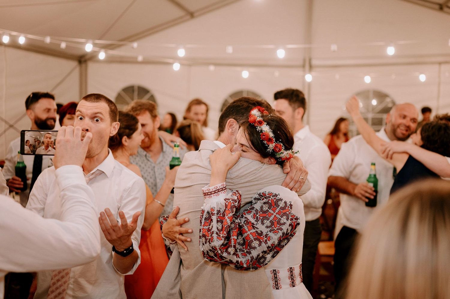 Joyful wedding celebration with guests dancing in tent venue.