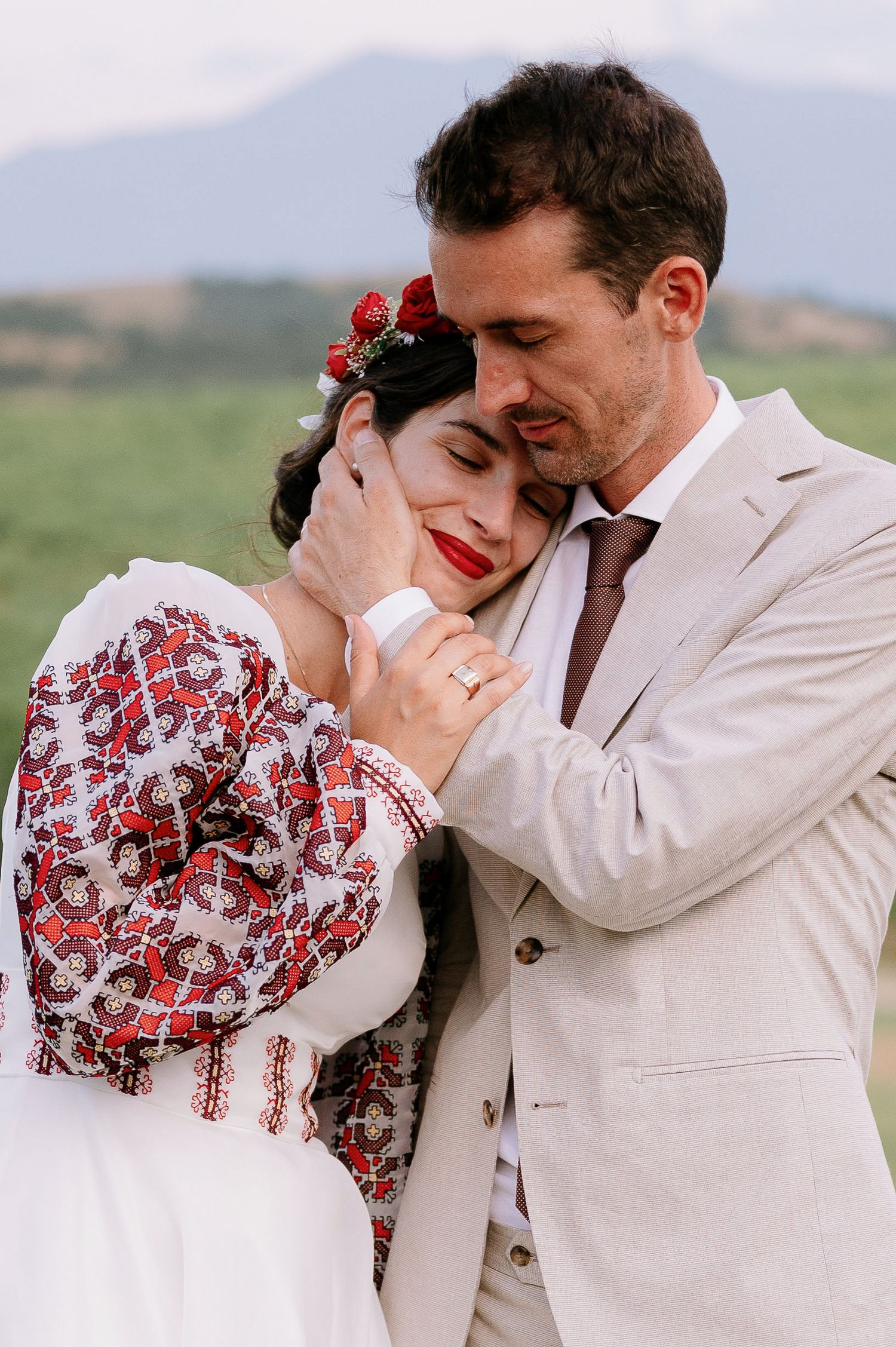 Intimate wedding portrait showing couple embracing in traditional attire against mountain landscape.