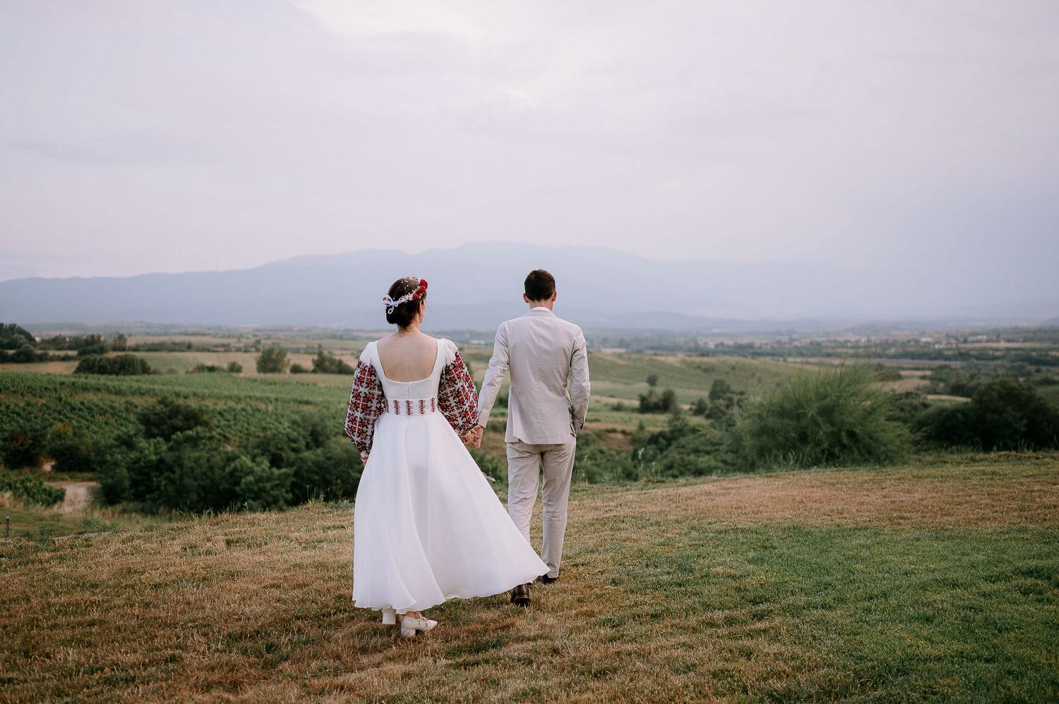 Couple in wedding attire standing together overlooking a scenic mountain landscape.