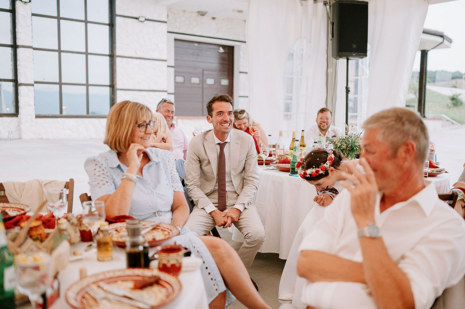 Guests laughing and celebrating at an indoor wedding reception with rustic industrial decor.