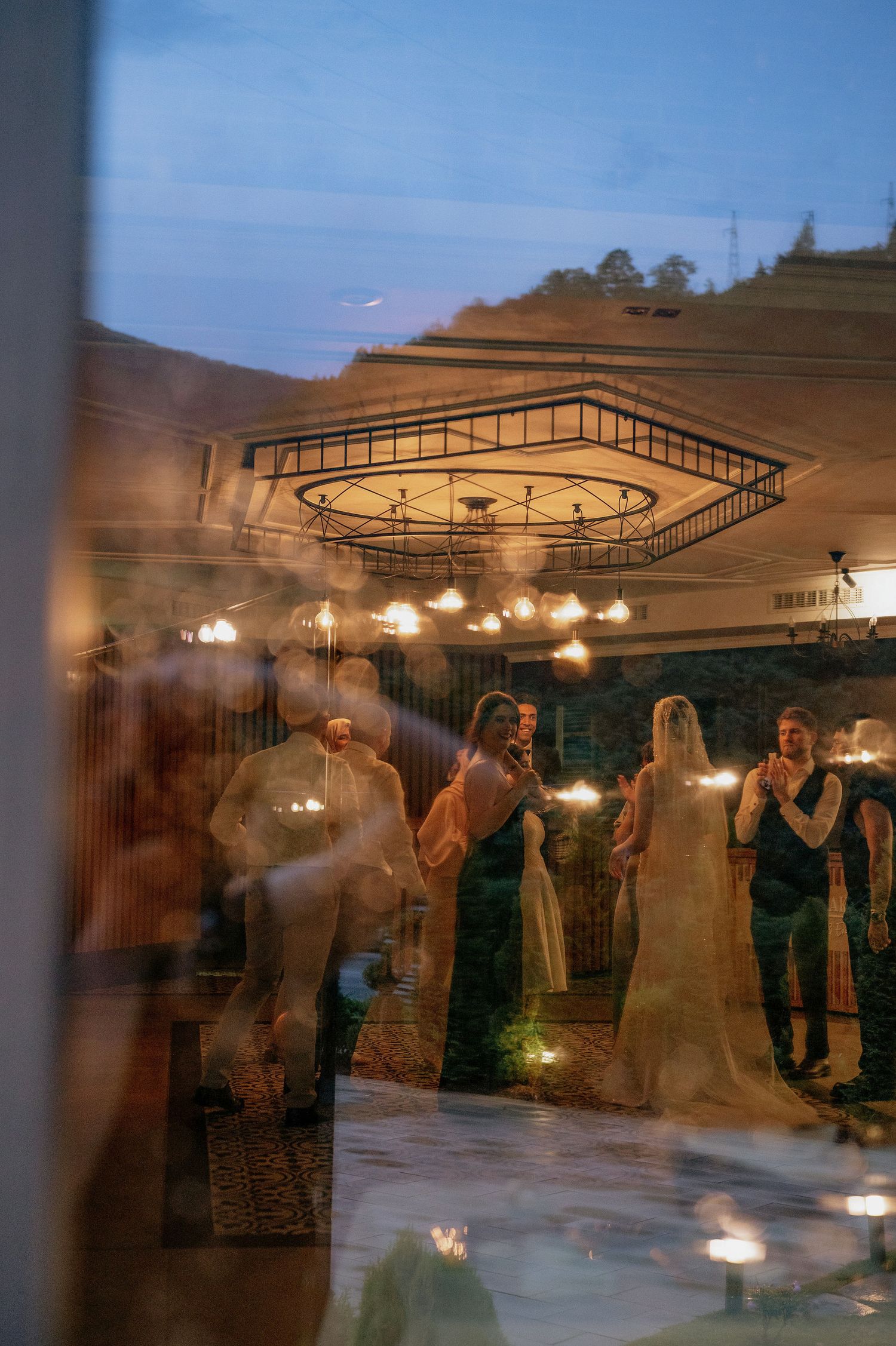 Evening wedding reception with guests dancing under illuminated outdoor pavilion.
