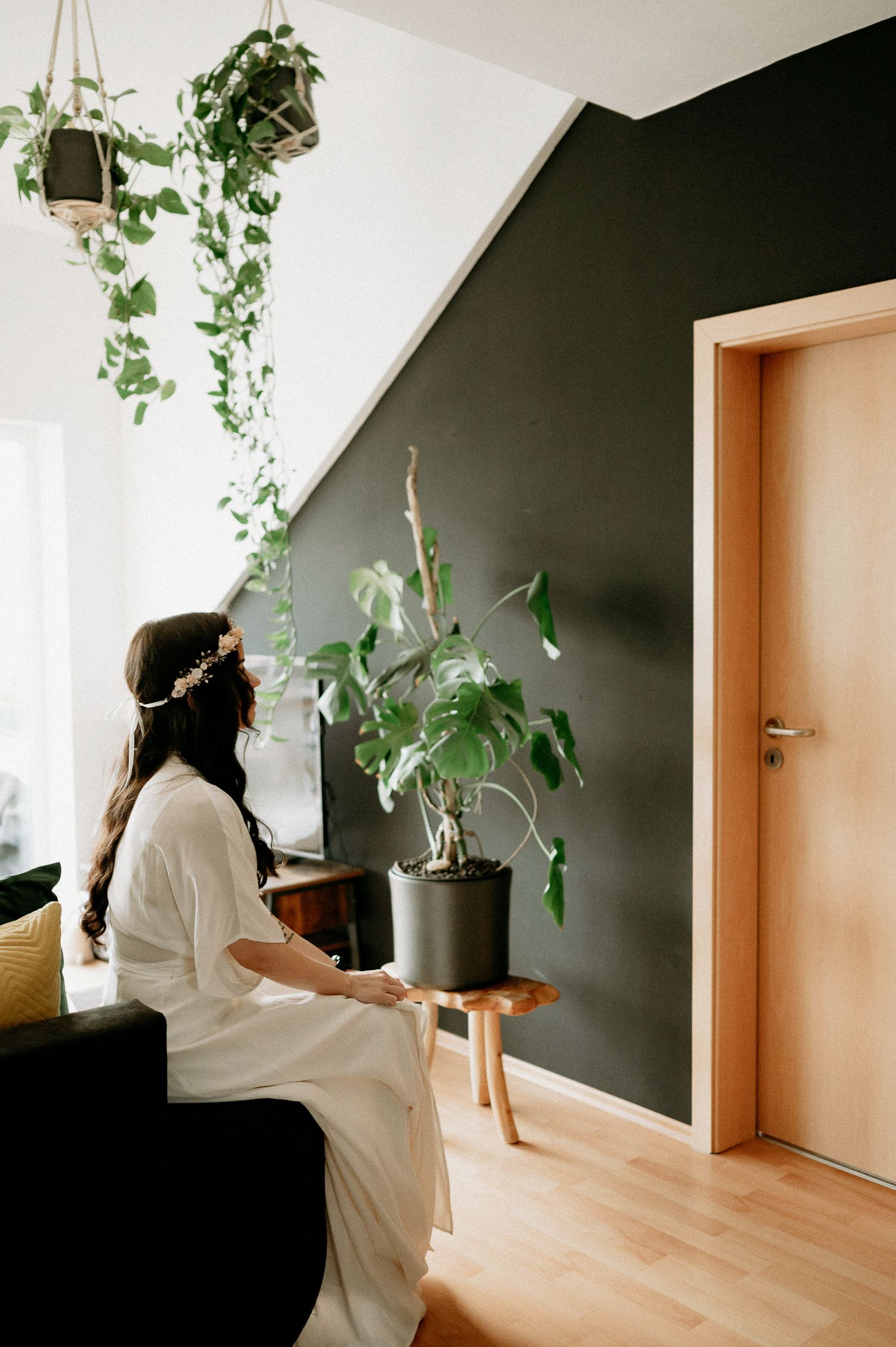 An interior space with hanging plants against a black accent wall and natural lighting.