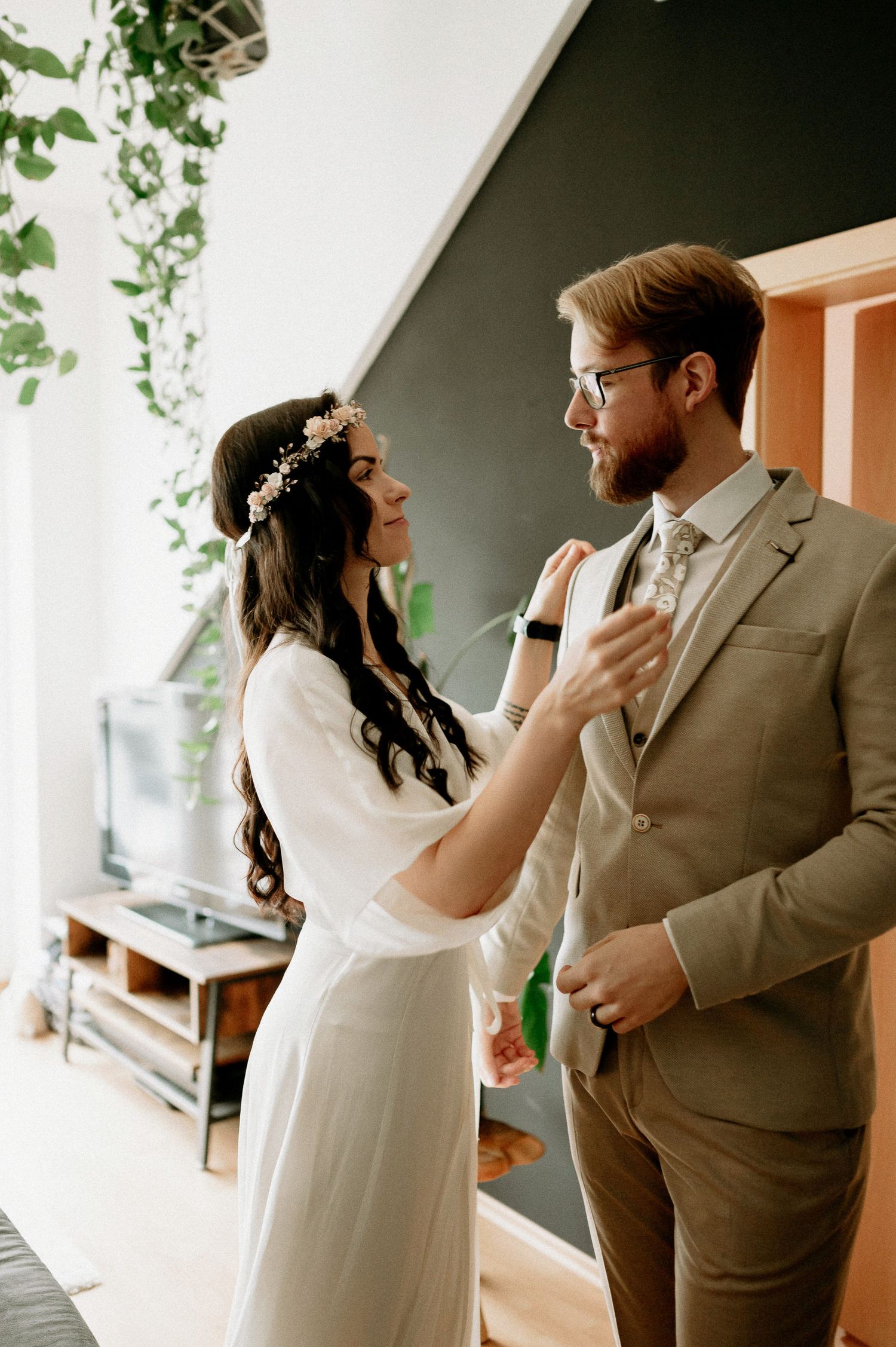 A couple sharing an emotional first look moment in a room with hanging plants.