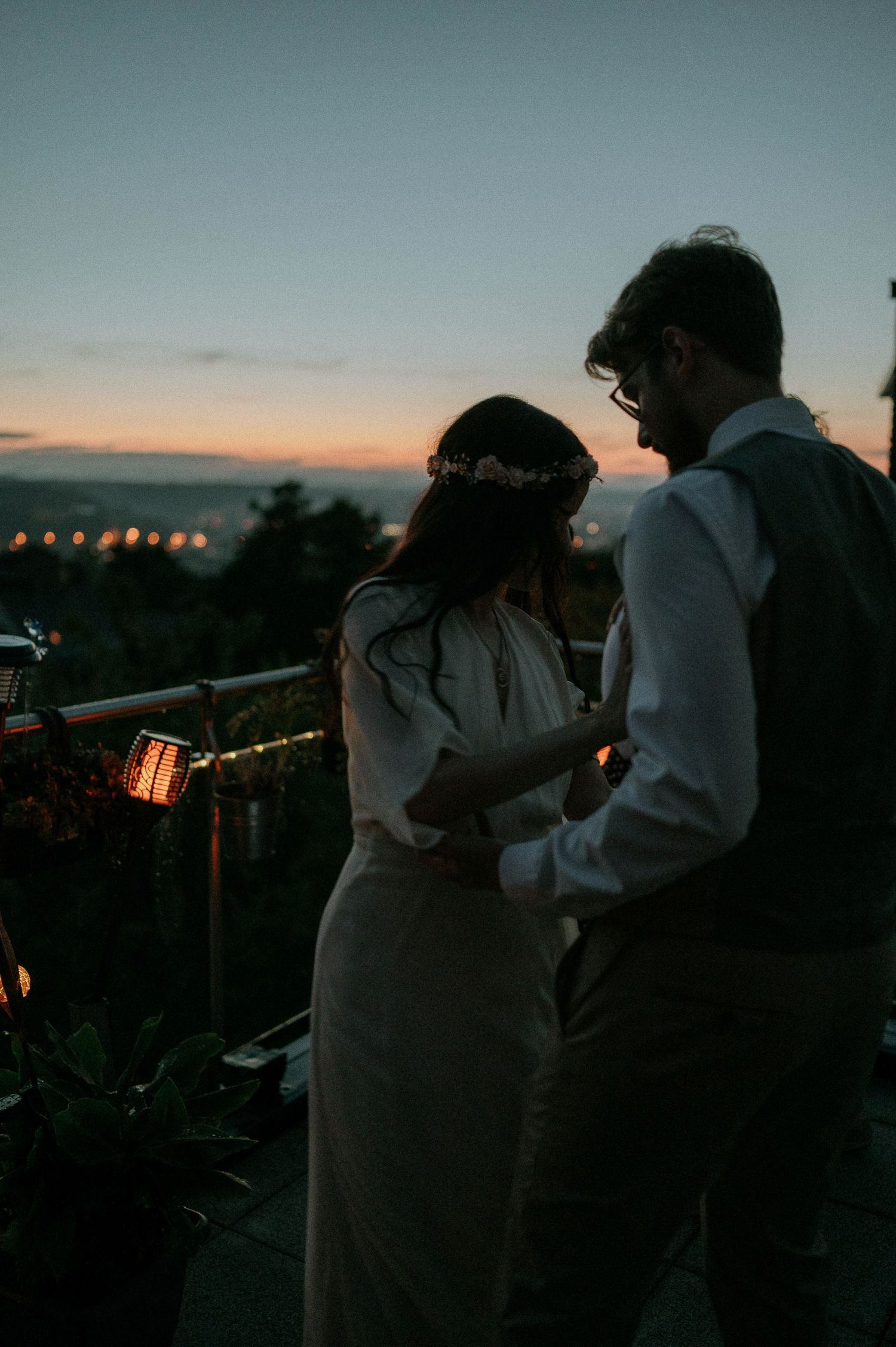 Small group gathering on outdoor terrace at twilight with city lights in background.